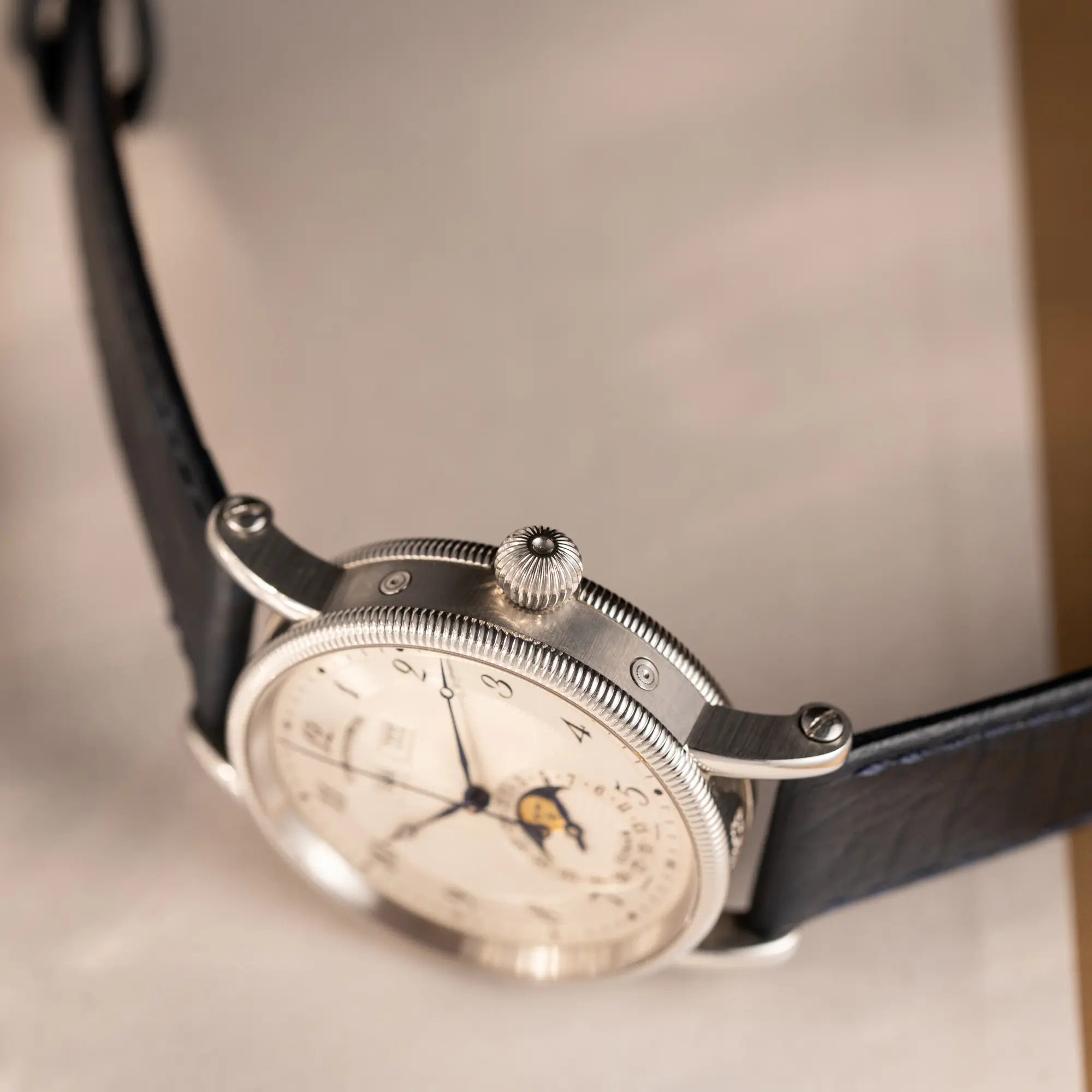 Produktfotografie der Chronoswiss Klassic Luna Mondphase CH9323 mit silbernem, guillochiertem Zifferblatt mit Kalenderanzeige auf 12 Uhr und einer Mondphase-Anzeige bei 6 Uhr zeigt die Aufzugskrone