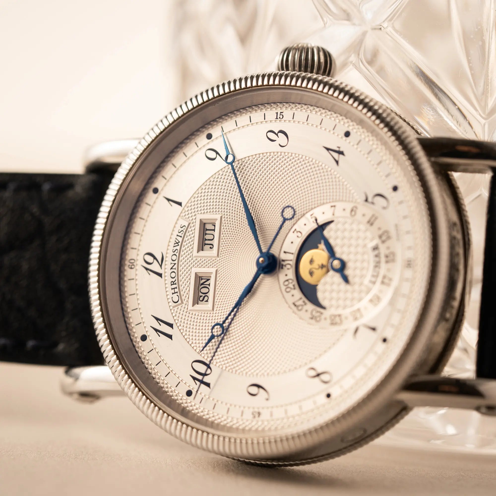 Produktfotografie der Chronoswiss Klassic Luna Mondphase CH9323 mit silbernem, guillochiertem Zifferblatt mit Kalenderanzeige auf 12 Uhr und einer Mondphase-Anzeige bei 6 Uhr