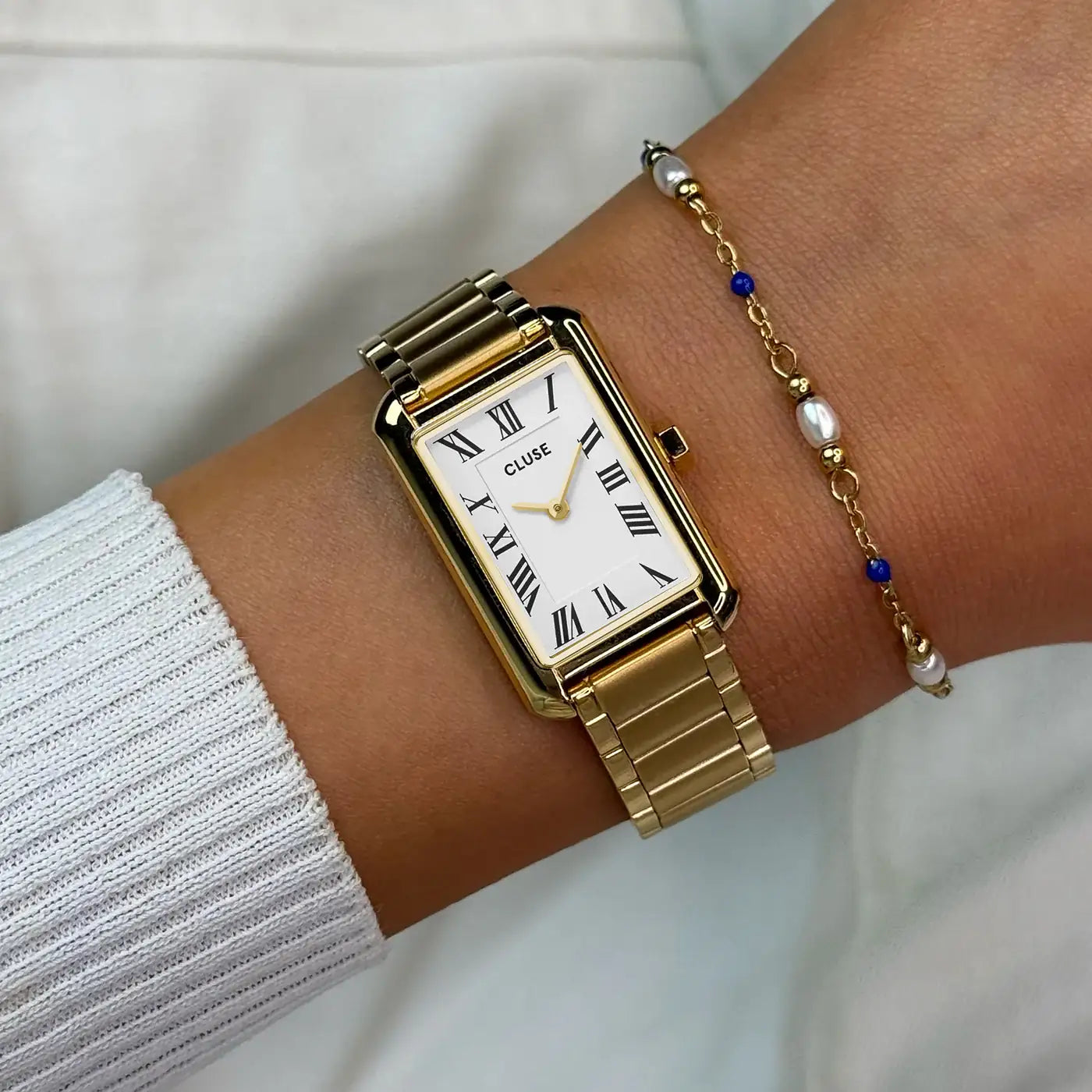 Wristshot mit der goldfarbenen Cluse Belisenna Damenuhr mit länglichem,  rechteckigem Gehäuse und weißem Zifferblatt mit römischen Indizes