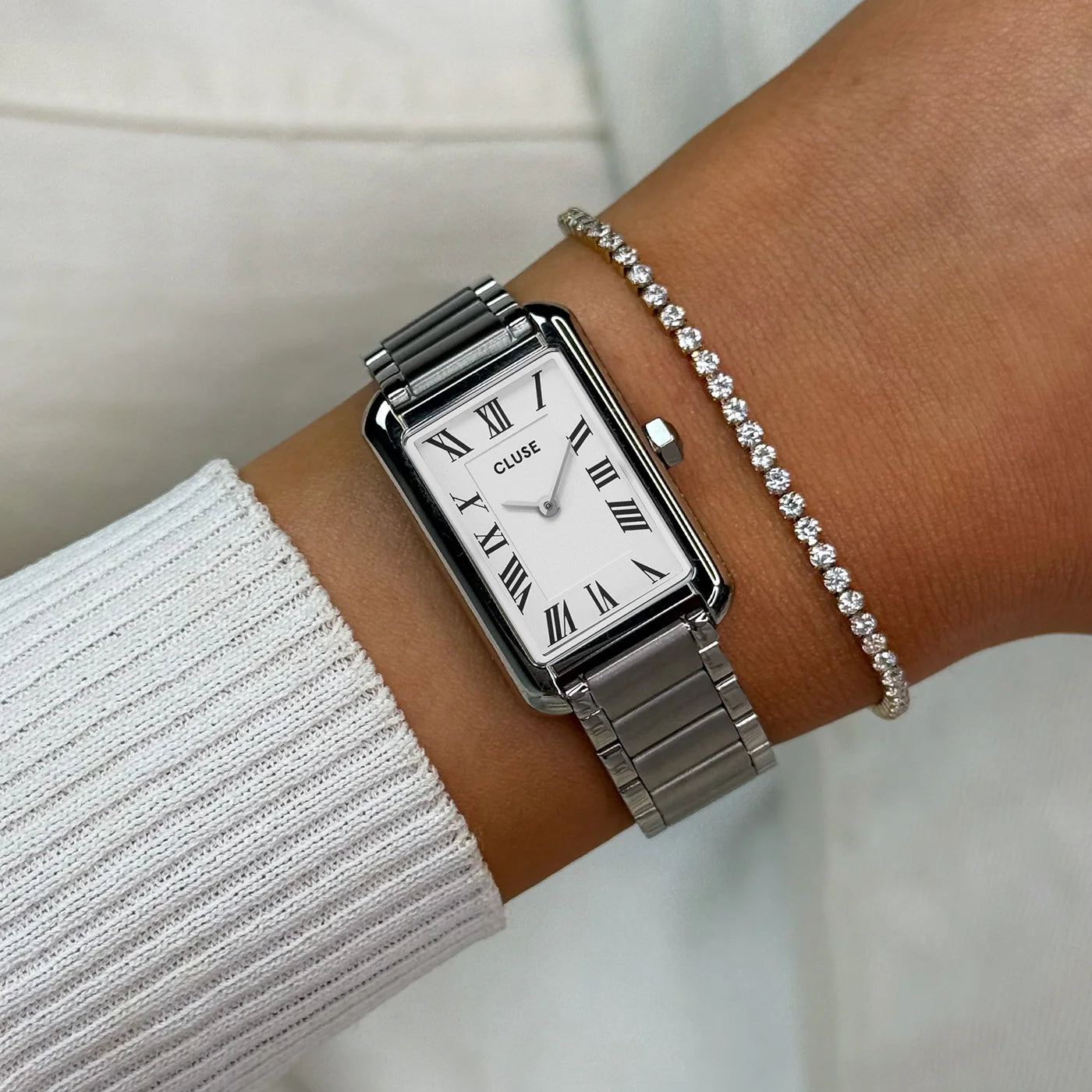 Wristshot mit der silberfarbenen Cluse Belisenna Damenuhr mit länglichem,  rechteckigem Gehäuse und weißem Zifferblatt mit römischen Indizes
