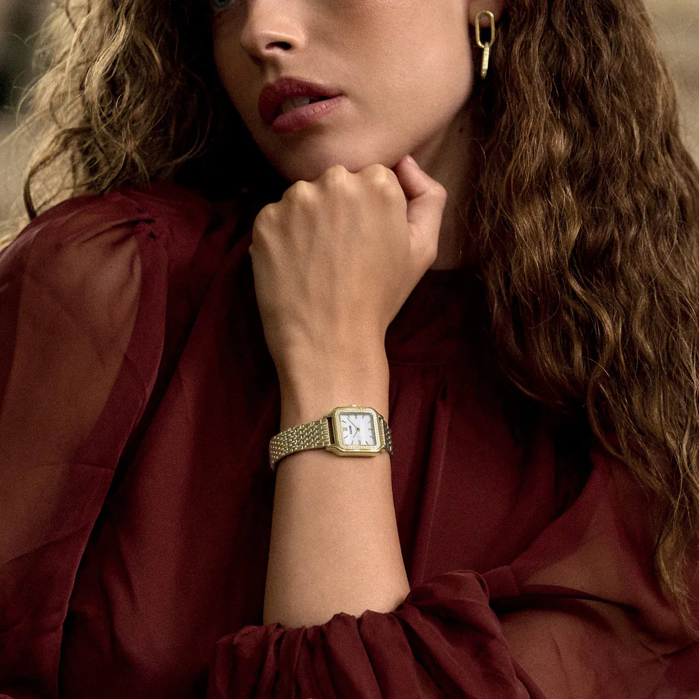 Frau trägt die goldfarbene Cluse Gracieuse Damenuhr CW11826 mit weißem Zifferblatt und einem Glassteinbesatz auf der Lünette an ihrem Handgelenk