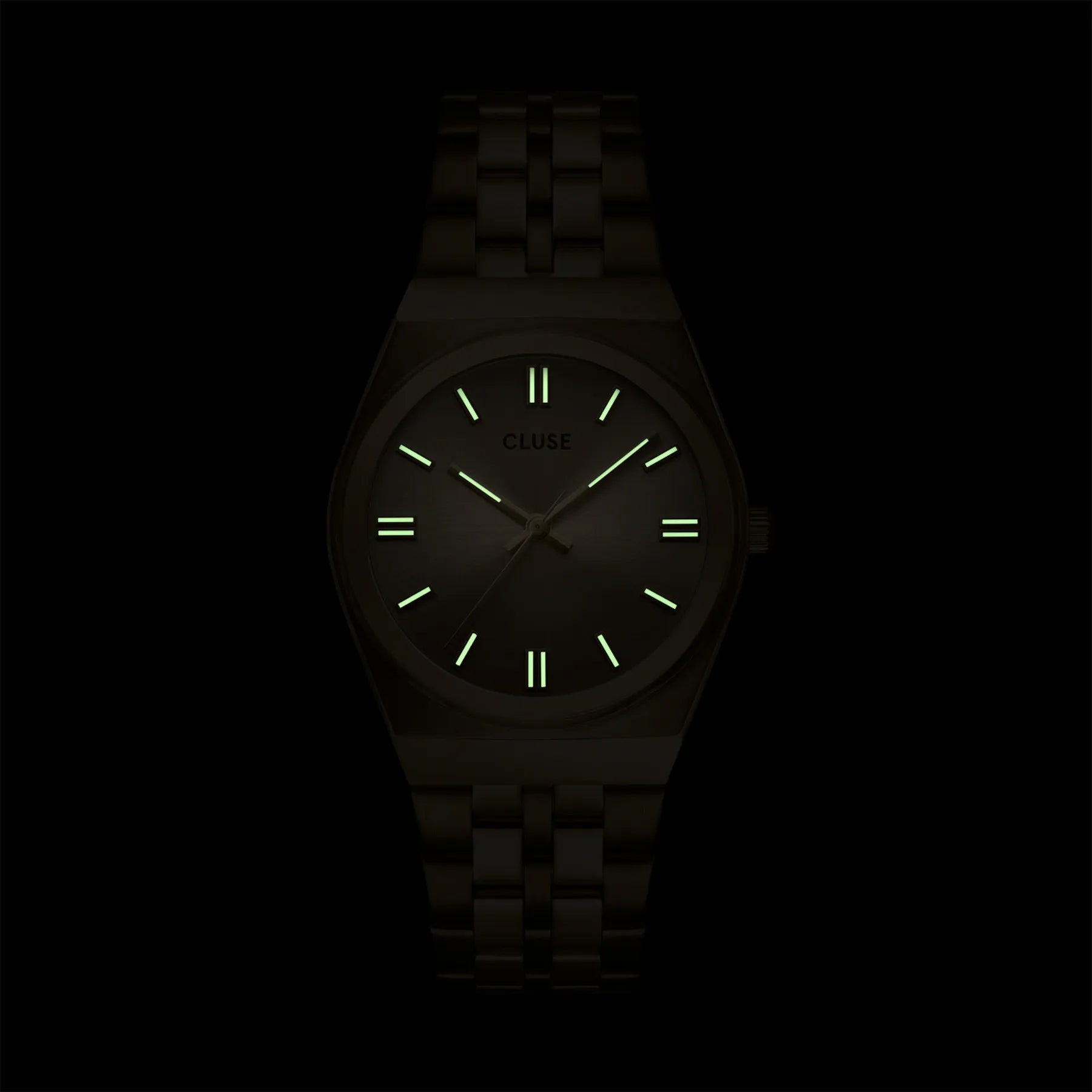 Blick auf das Zifferblatt mit leuchtenden Indizes und Zeigern der  goldfarbenen Cluse Damenuhr Retro 70s der Referenz CW35104 mit integriertem Armband und goldfarbenem Zifferblatt