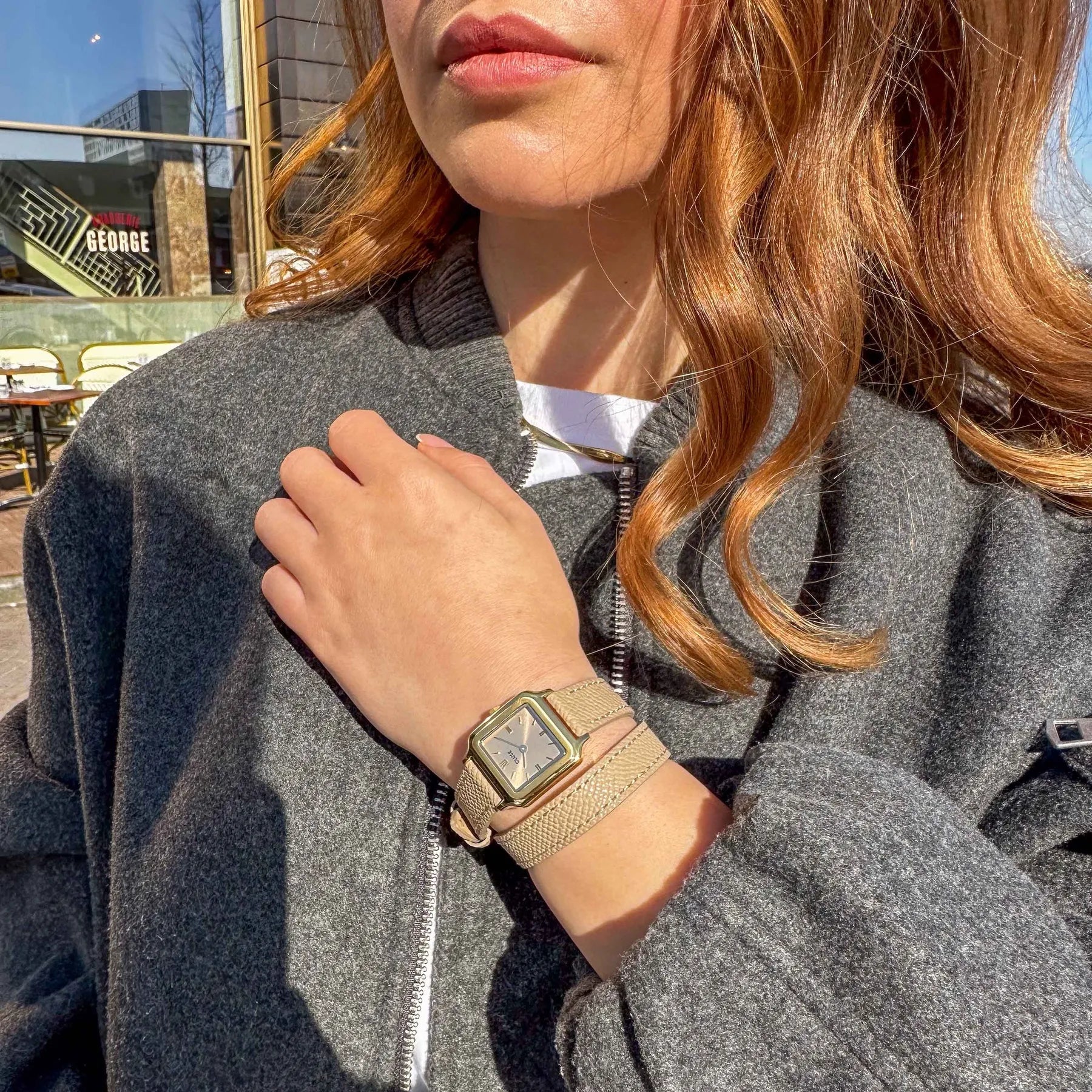 Lifestyleshot einer Frau mit der der goldfarbenen Cluse Gracieuse Petite Damenuhr mit rechteckigem Gehäuse und beigem/bronze-farbenem  Zifferblatt an einem Doppel-Armband aus Leder im gleichen Farbton wie das Zifferblatt