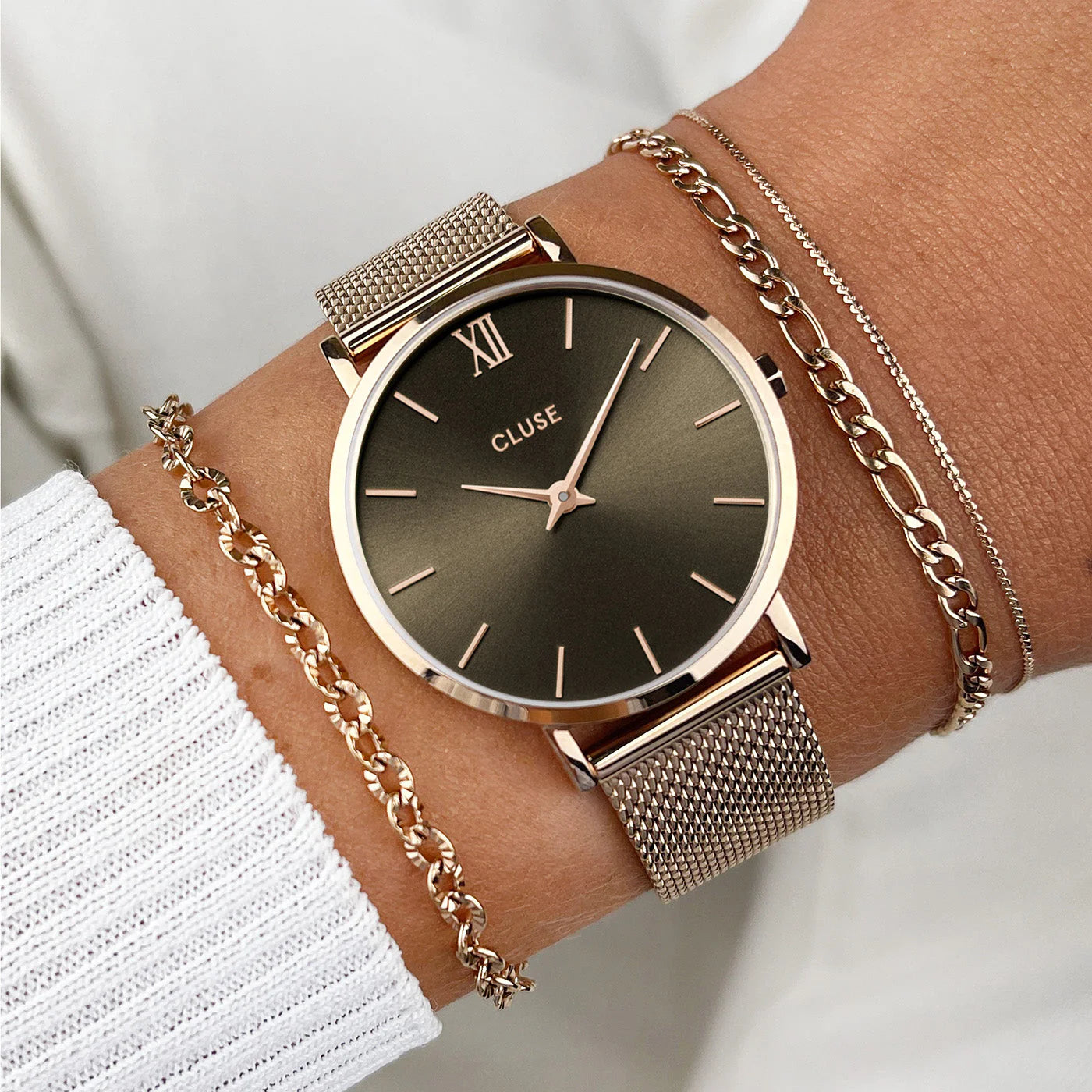 Frau trägt die Cluse Stahl-Uhr "Minuit Mesh" in roségoldener Farbe mit einem grau-brauen Zifferblatt an Ihrem Handgelenk