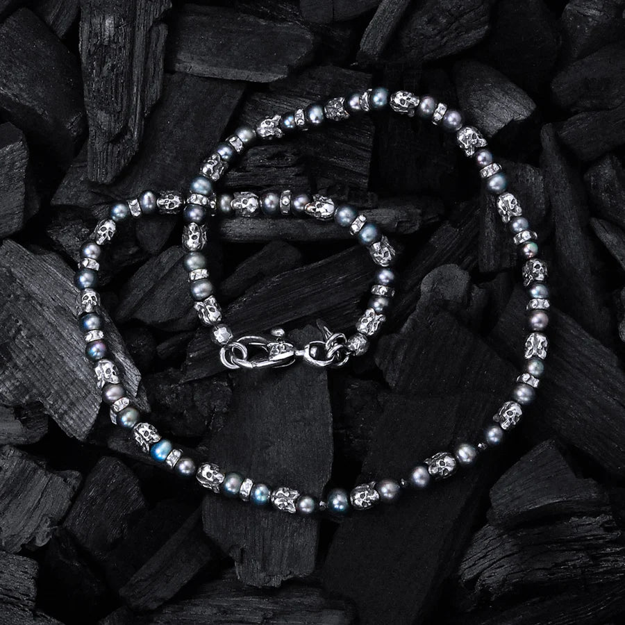 Produktofografie der Elfcraft Halskette  mit schwarzen Perlen und silbernen Elementen im Totenkopf, während das Collier auf schwarzer Holzkohle liegt