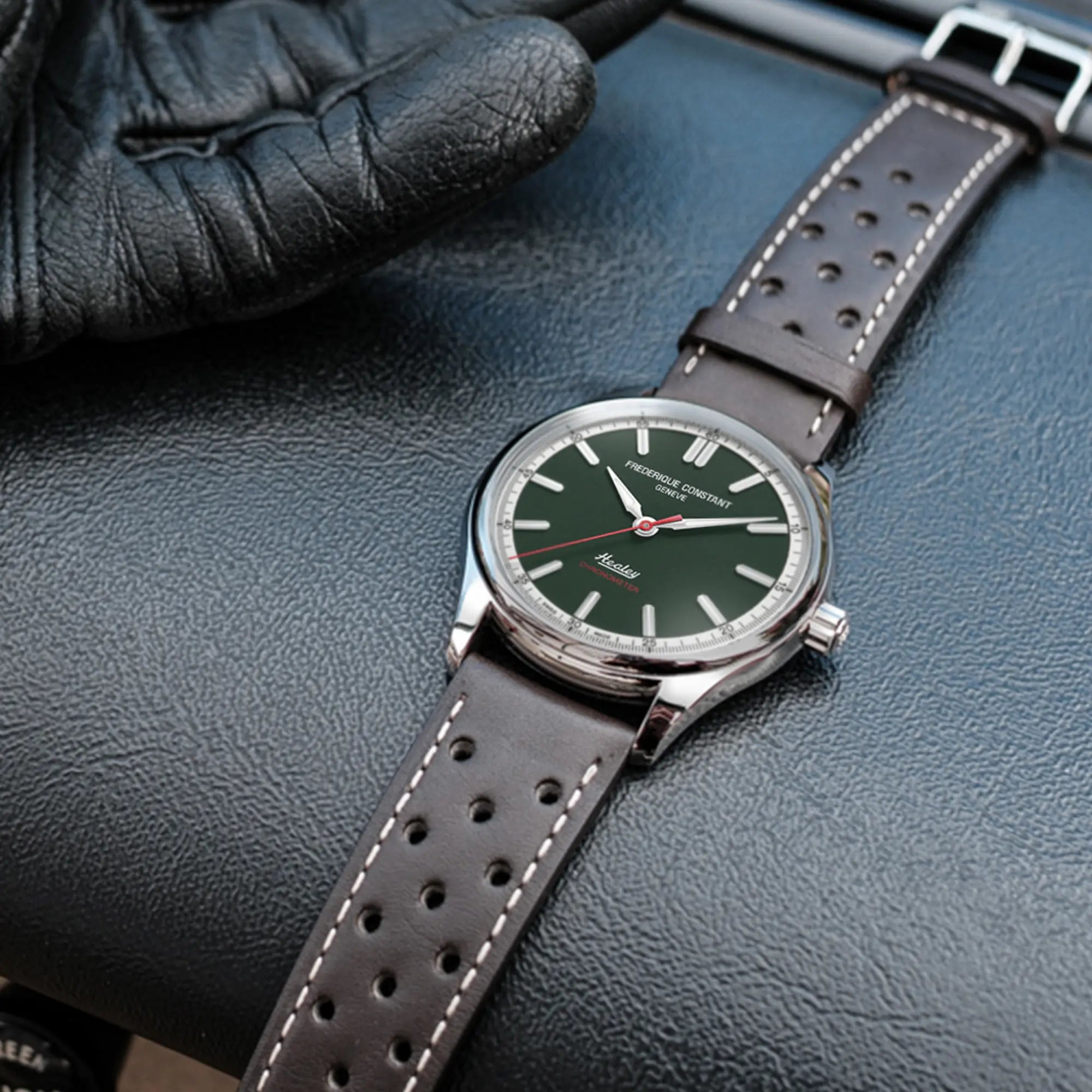 Produktfotografie der "Vintage Rally Healey" Uhr von Frederique Constant aus der Classics Kollektion mit einem dunkelgrünem Zifferblatt und einem braunen Lederarmband im Racing-Look, während die Uhr auf einem schwarzen Leder-Armaturenbrett liegt