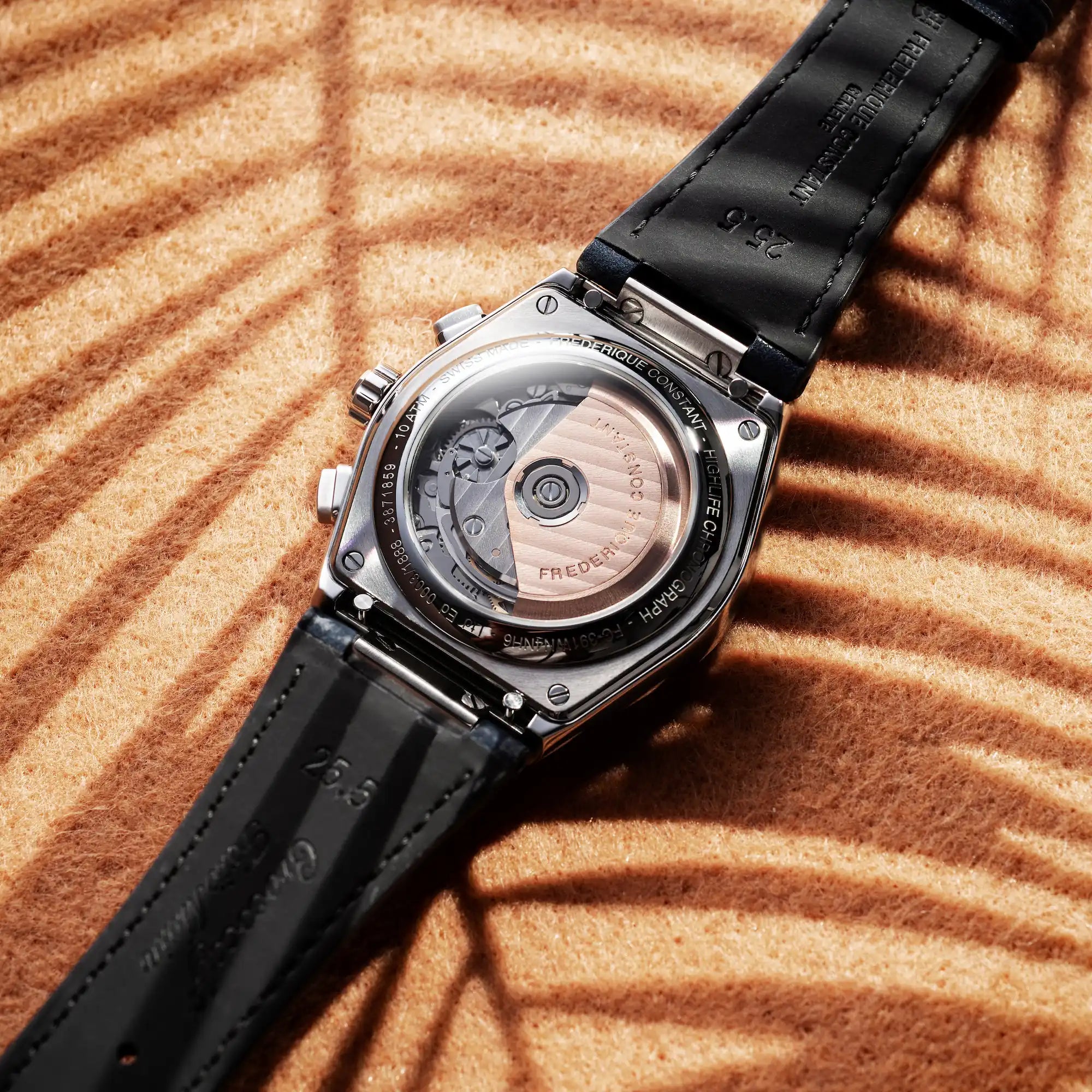 Detailaufnahme des Gehäuseboden des Automatic Chronographen mit blauen Akzenten und einem dunkelblauen Lederarmband von Frederique Constant aus der Highlife-Kollektion auf einem orangenen Hintergrund