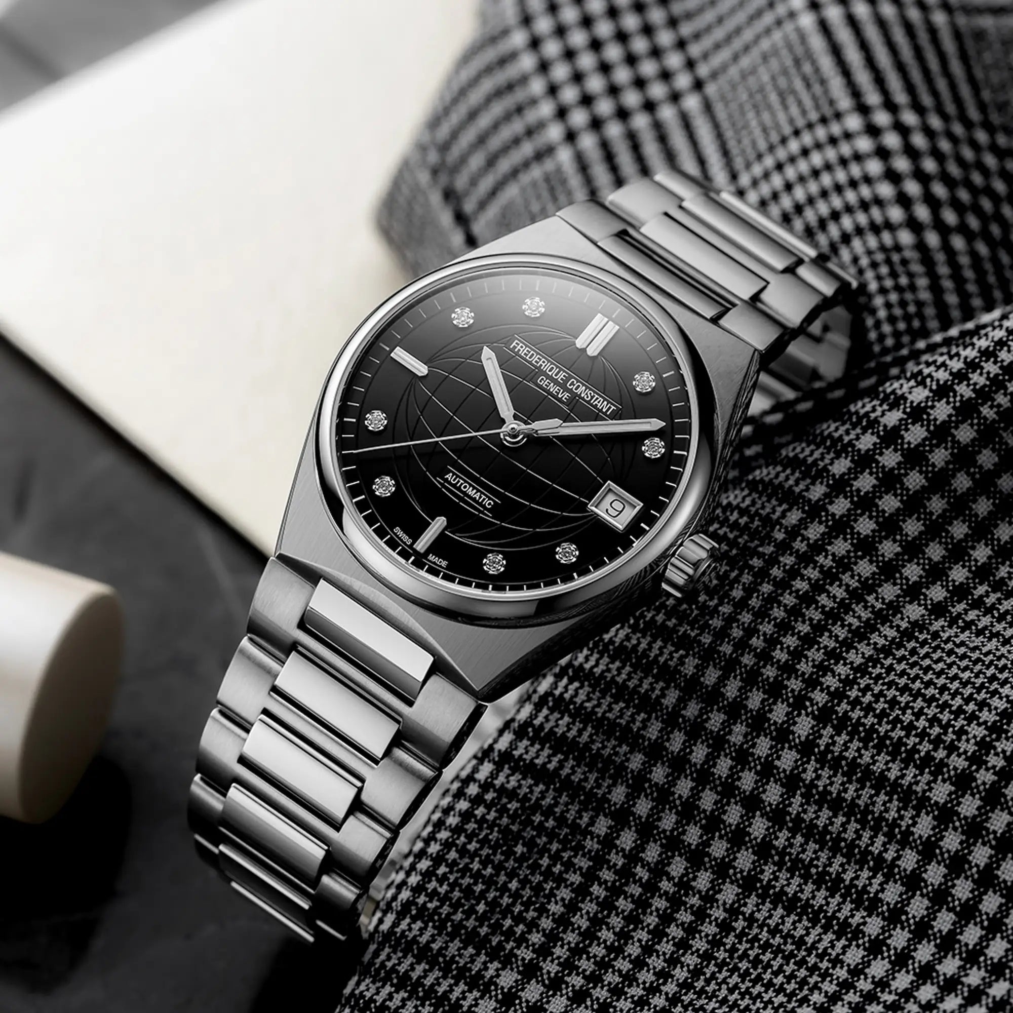 Produktfotografie der Frederique Constant Uhr "Highlife Ladies Automatic" mit einem schwarzen Zifferblatt mit Diamant-Indizes und Edelstahl-Gehäuse auf einem schwarz-weiß karierten Stofftuch 