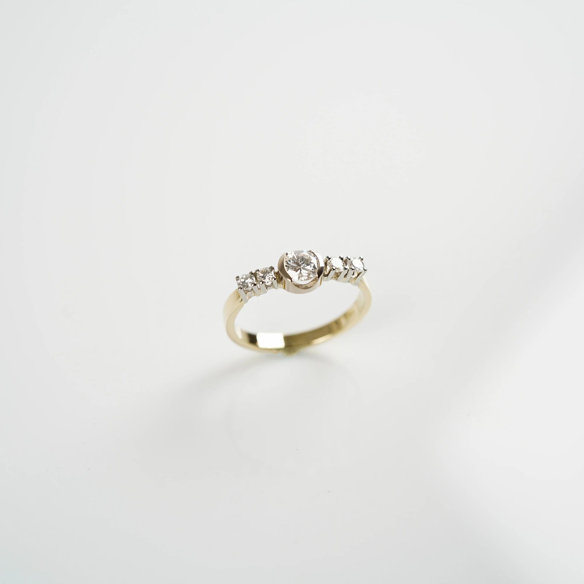 Produktfoto mit leicht schrägem Blick von Oben auf den gelbgoldenen Ring mit 5 gefassten Diamanten auf der Ringschiene, wovon der zentrale Stein der Größte ist