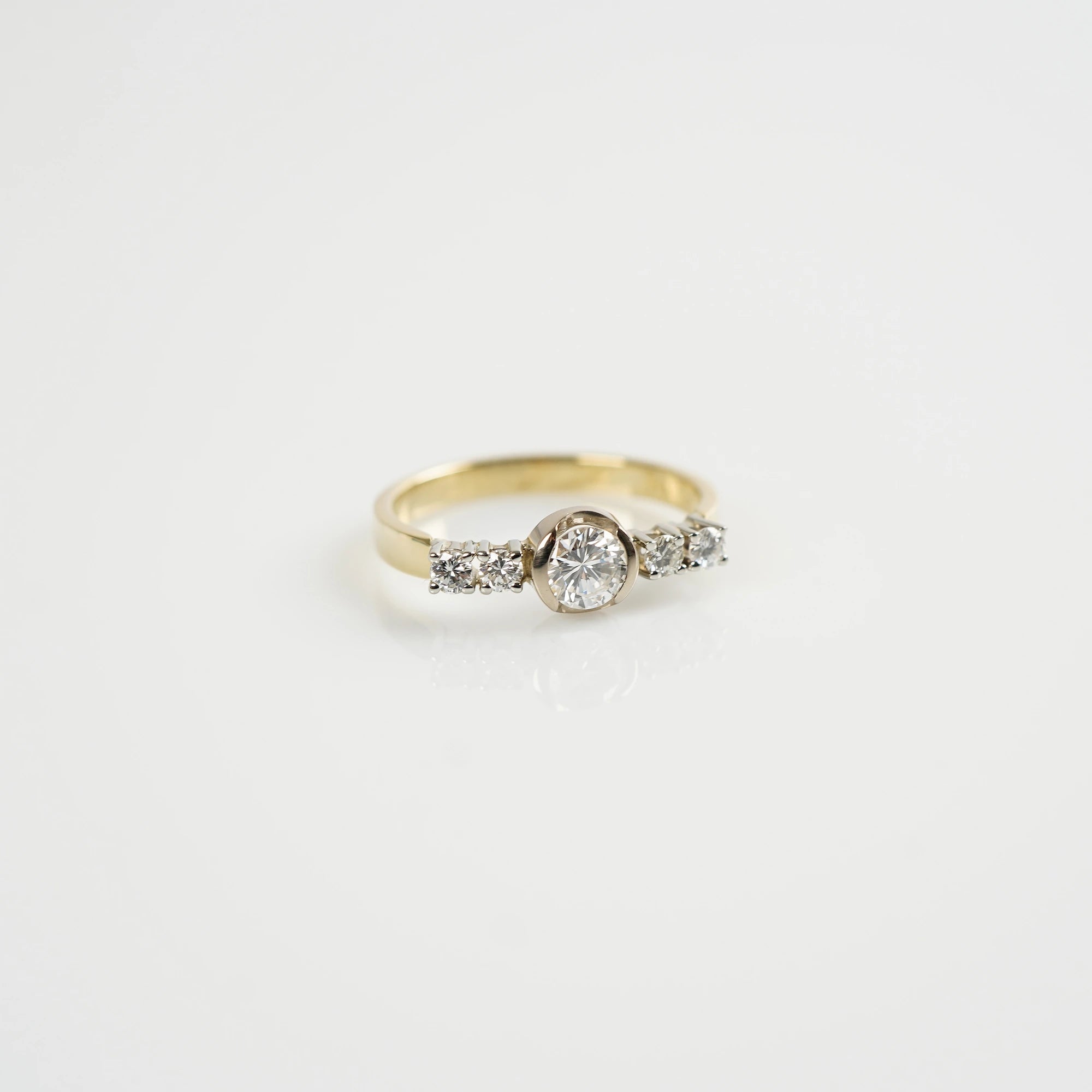 Produktfoto des liegenden, gelbgoldenen Ring mit 5 gefassten Diamanten auf der Ringschiene, wovon der zentrale Stein der Größte ist