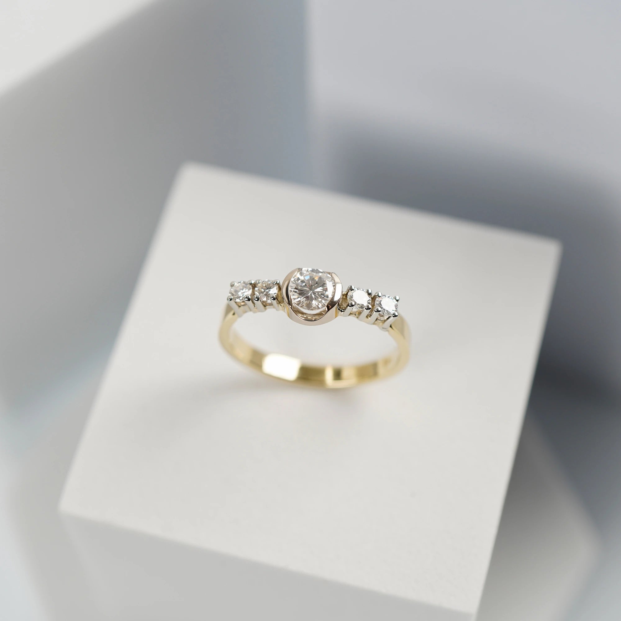 Produktfoto mit Blick von Oben auf den gelbgoldenen Ring mit 5 gefassten Diamanten auf der Ringschiene, wovon der zentrale Stein der Größte ist