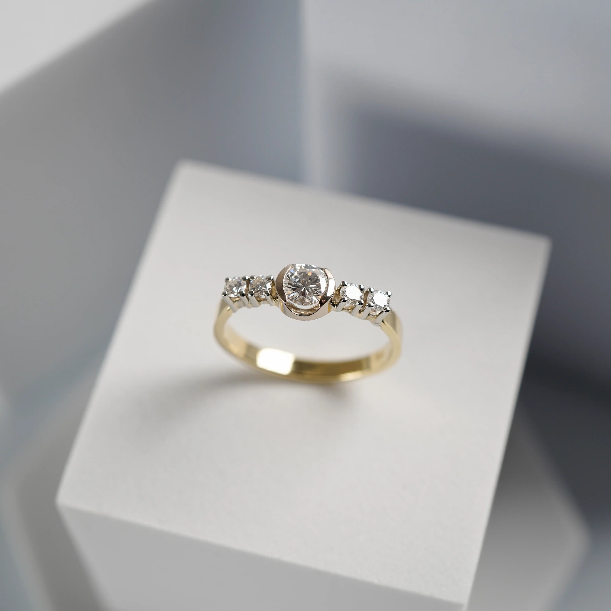 Produktfotografie des gelbgoldenen Ring mit 5 gefassten Diamanten auf der Ringschiene, wovon der zentrale Stein der Größte ist