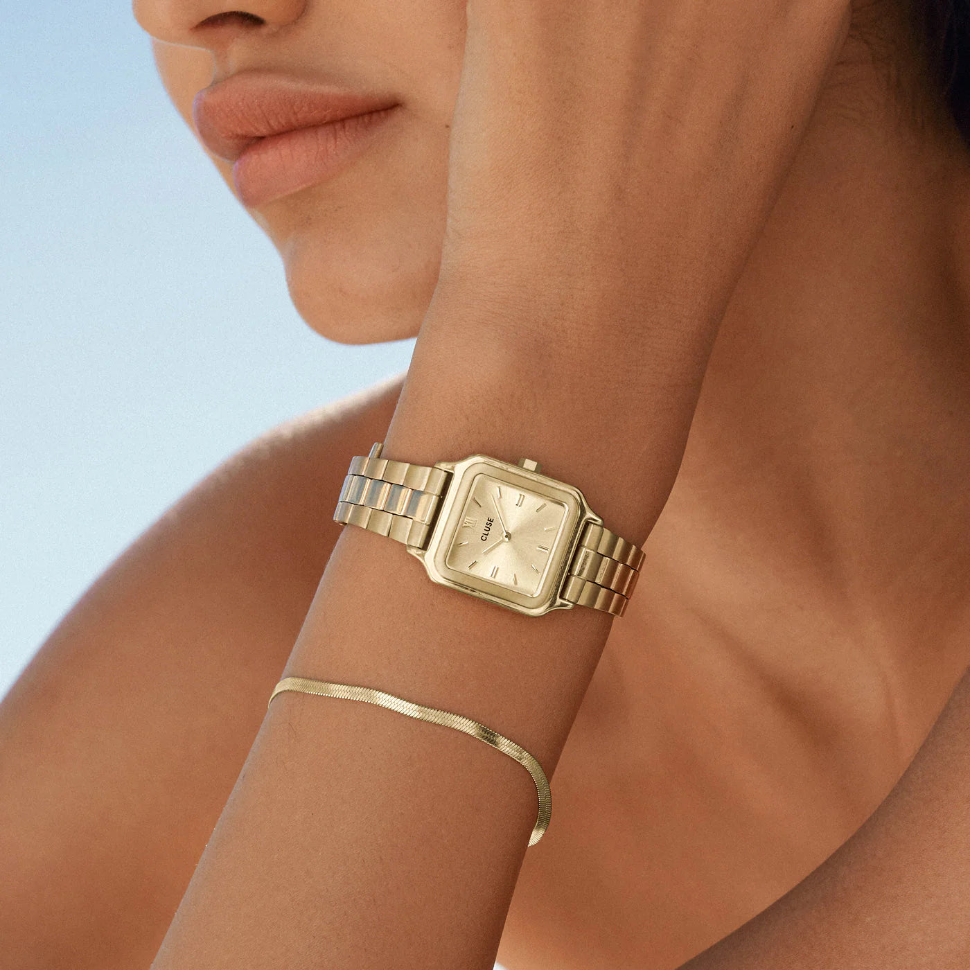 Frau kombiniert die Cluse Stahl-Uhr "Gracieuse Petite" mit einem gelbgold-farbenem Gehäuse und Zifferblatt mit einem passenden goldenen Armband