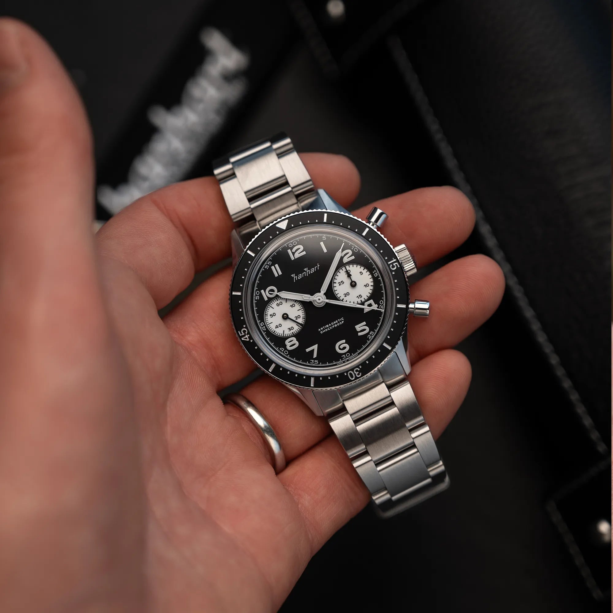 Mann hält die Hanhart 415 ES Chronographs mit dem Reverse-Panda-Zifferblatt in Schwarz mit weißen Sub-Dials am Edelstahlarmband und präsentiert die Uhr in die Kamera