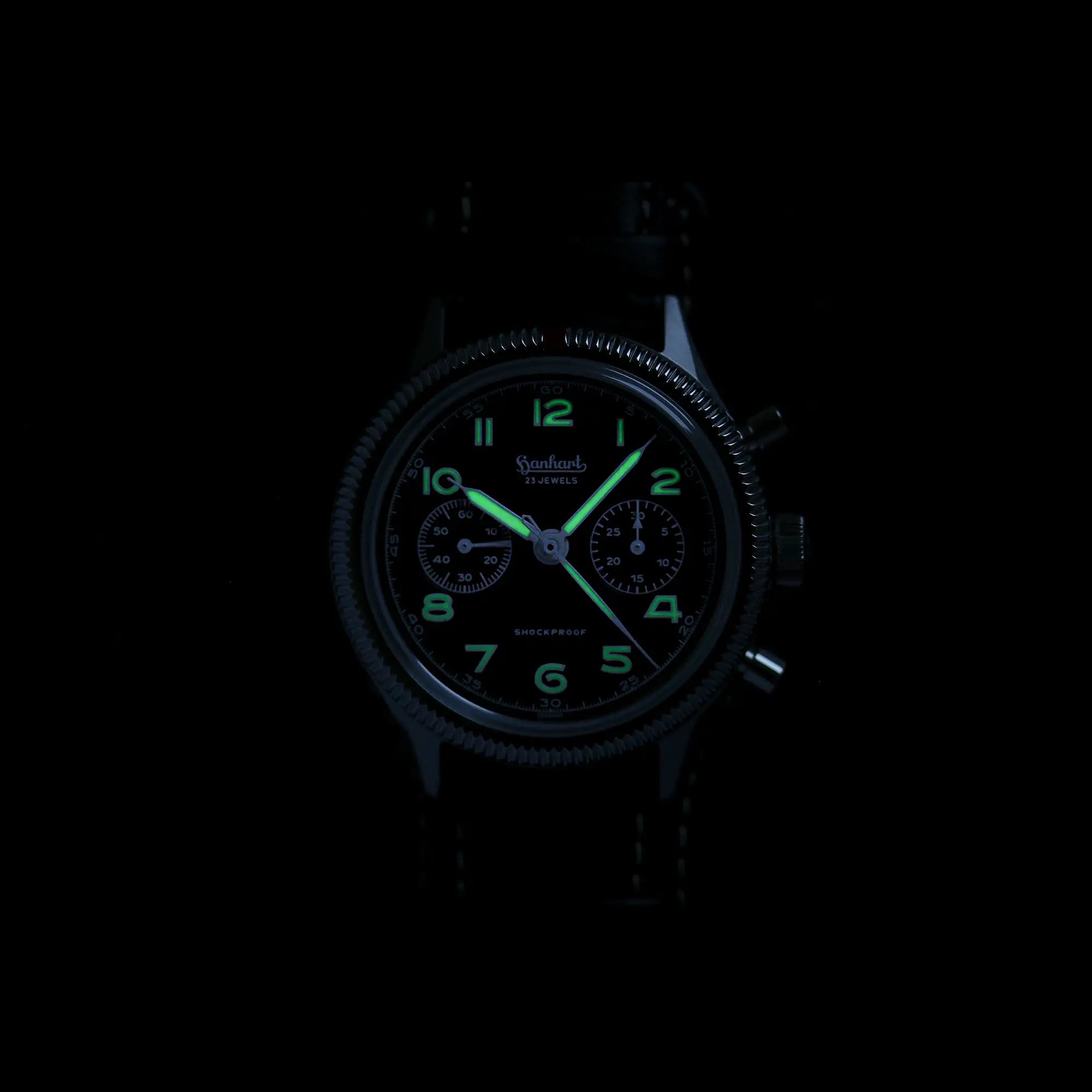 Fotografie der mechanischen Uhr "417 ES" aus der Pioneer Kollektion bei Nacht, mit gut sichtbarer grüner Leuchtmassemit Fokus auf dem traditionellen Hanhart-Logo