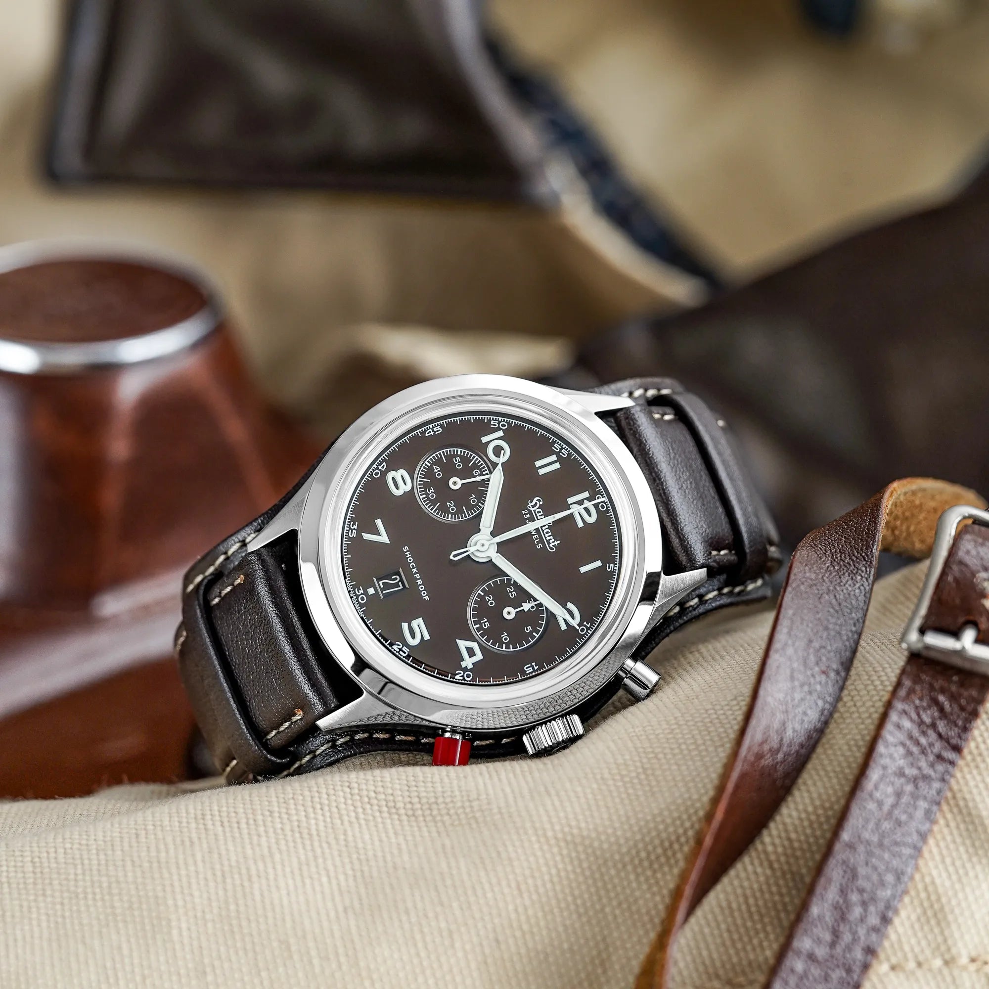 Produktfotografie der Hanhart 417 ES Mokka Limited Edition mit einem braunem Zifferblatt an einem passenden braunem Lederband mit Unterlage