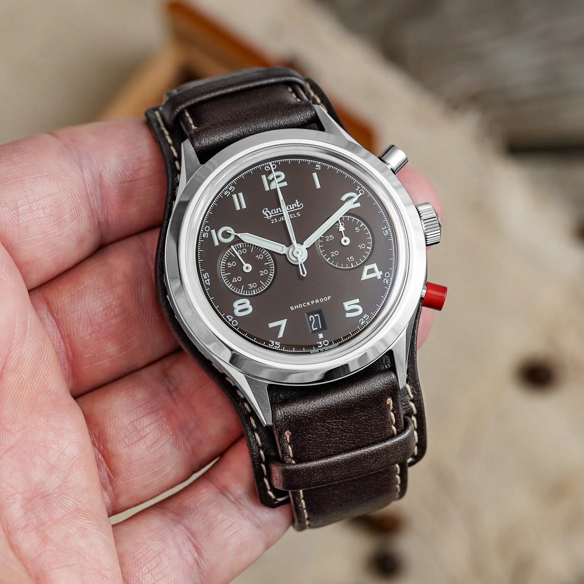 Mann hält die Hanhart 417 ES Mokka Limited Edition mit einem braunem Zifferblatt an einem passenden braunem Lederband mit Unterlage in seiner Hand und präsentiert die Uhr in die Kamera