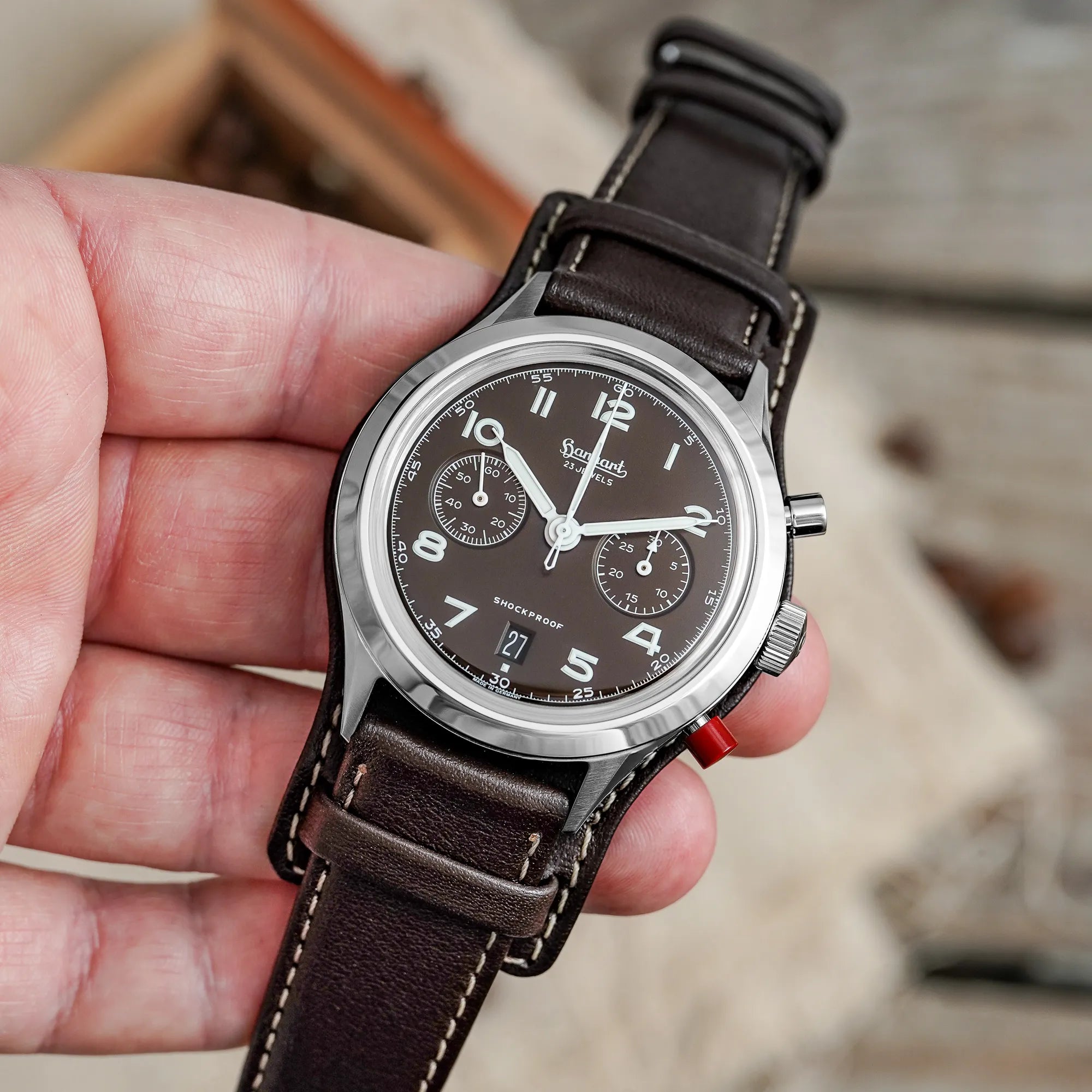 Mann hält die Hanhart 417 ES Mokka Limited Edition mit einem braunem Zifferblatt an einem passenden braunem Lederband mit Unterlage in seiner Hand