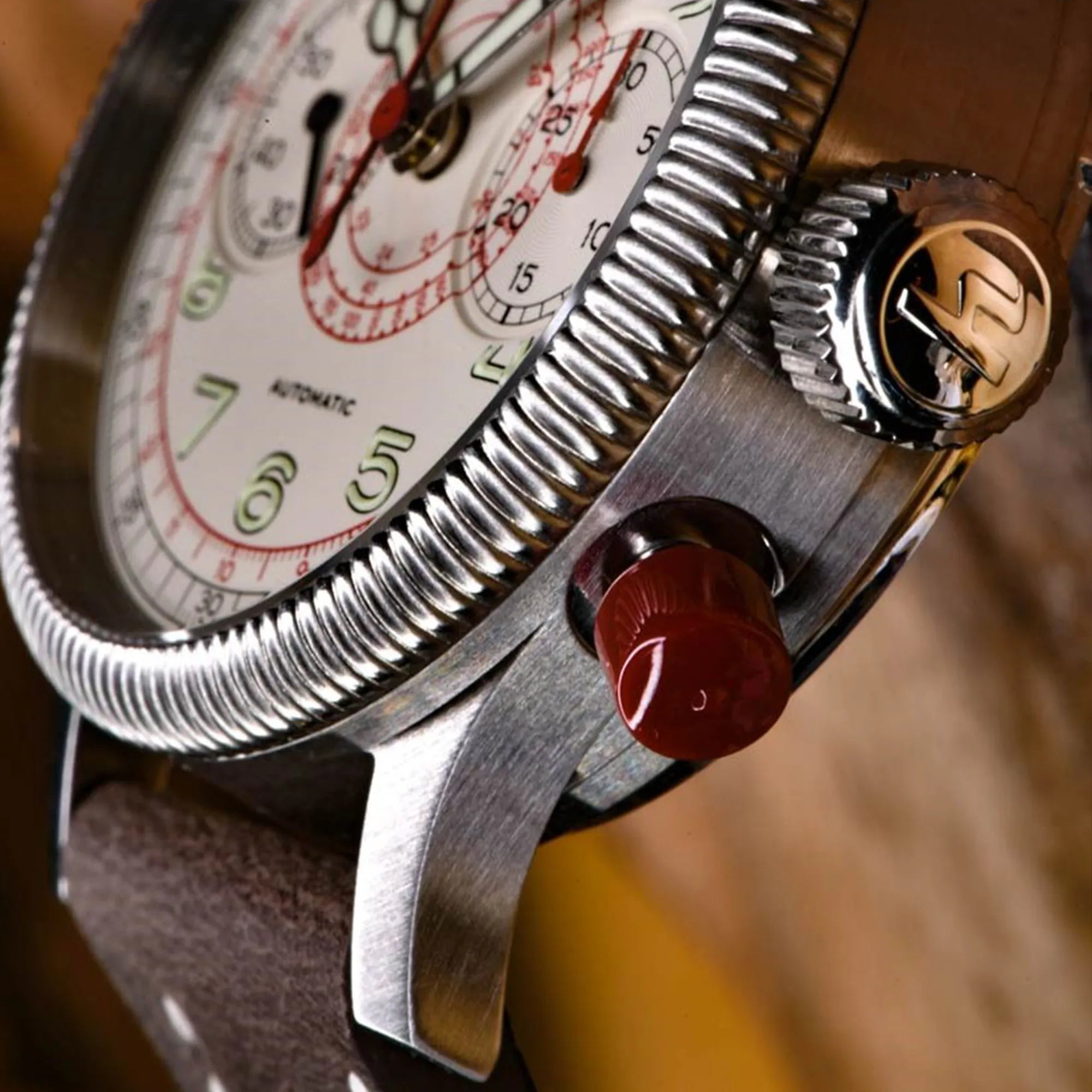 Detailaufnahme des roten Drückers und der kannelierten Lünette von der Hanhart Pioneer TachyTele Chronograph mit altweißem Zifferblatt und rot gehaltener Tachymeter-Skala und Telemeter-Skala am braunen Kalbslederband mit Niete