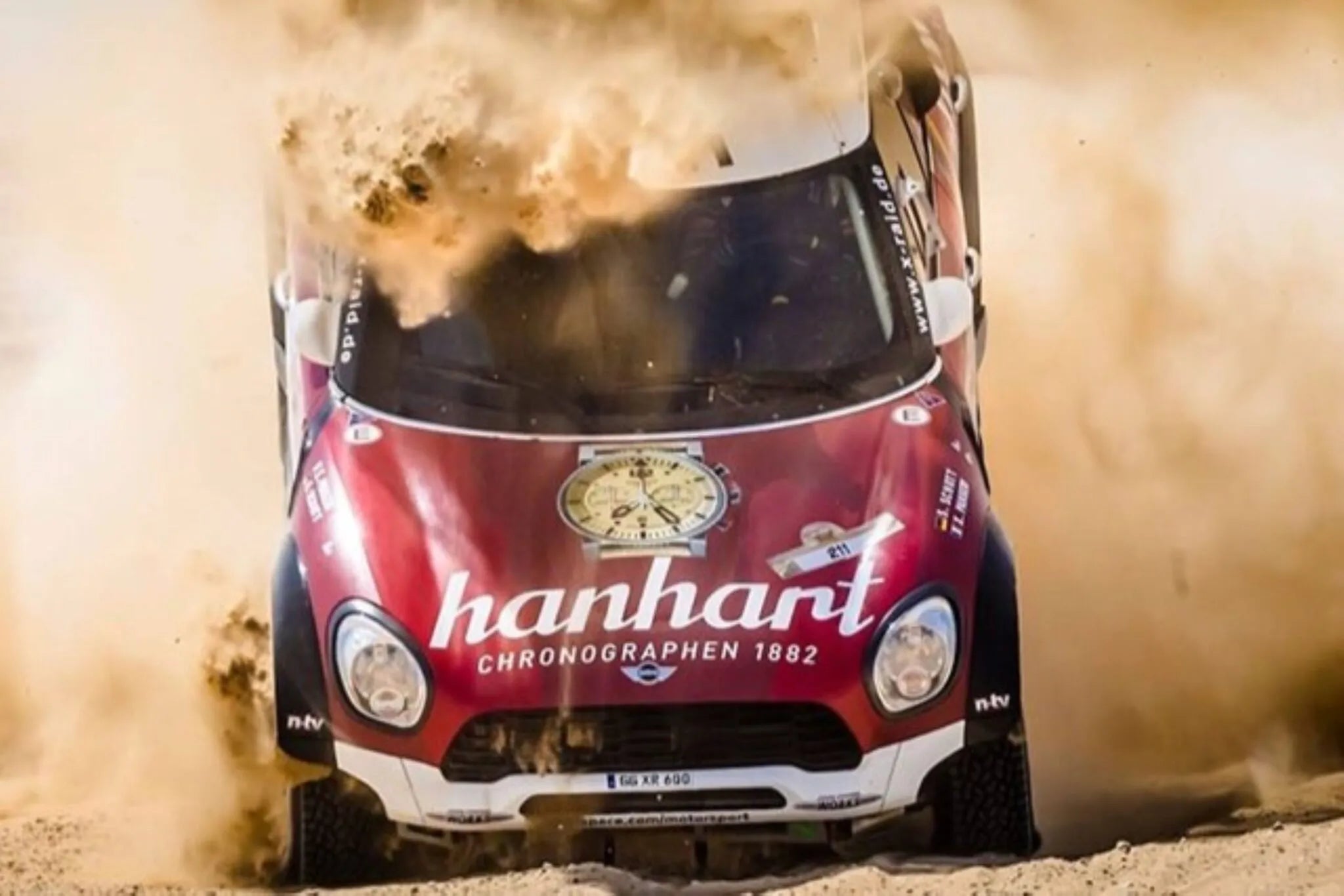 Roter Mini Cooper als Rally-Auto mit Hanhart-Werbung und einem sandfarbenen Primus-Modell auf der Motorhaube