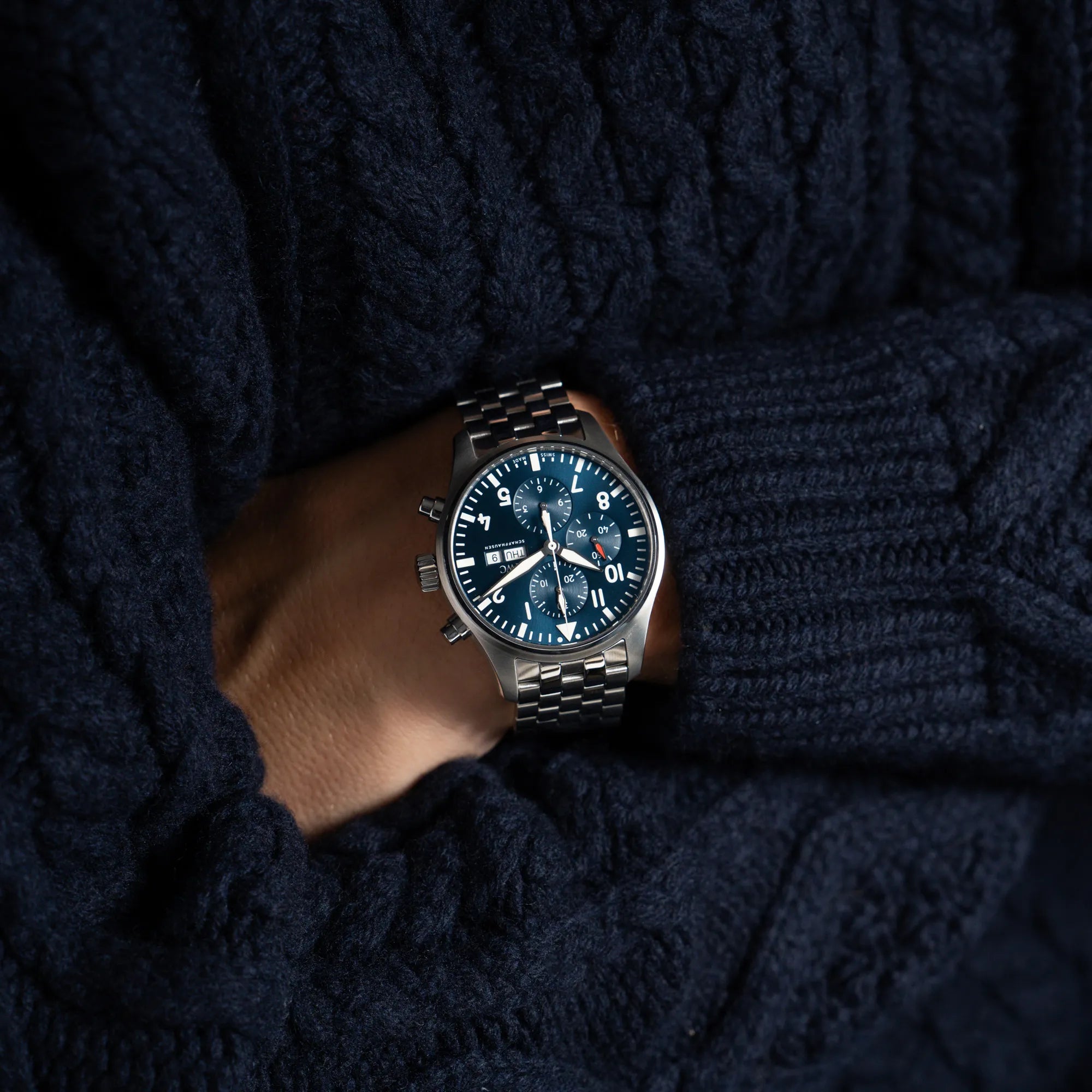 Mann in blauem Strickpullover hat den IWC Pilot Chronograph "Le Petit Prince" IW377717 mit 43 mm Gehäuse und blauem Zifferblatt am Edelstahl-Armband am Handegelenk