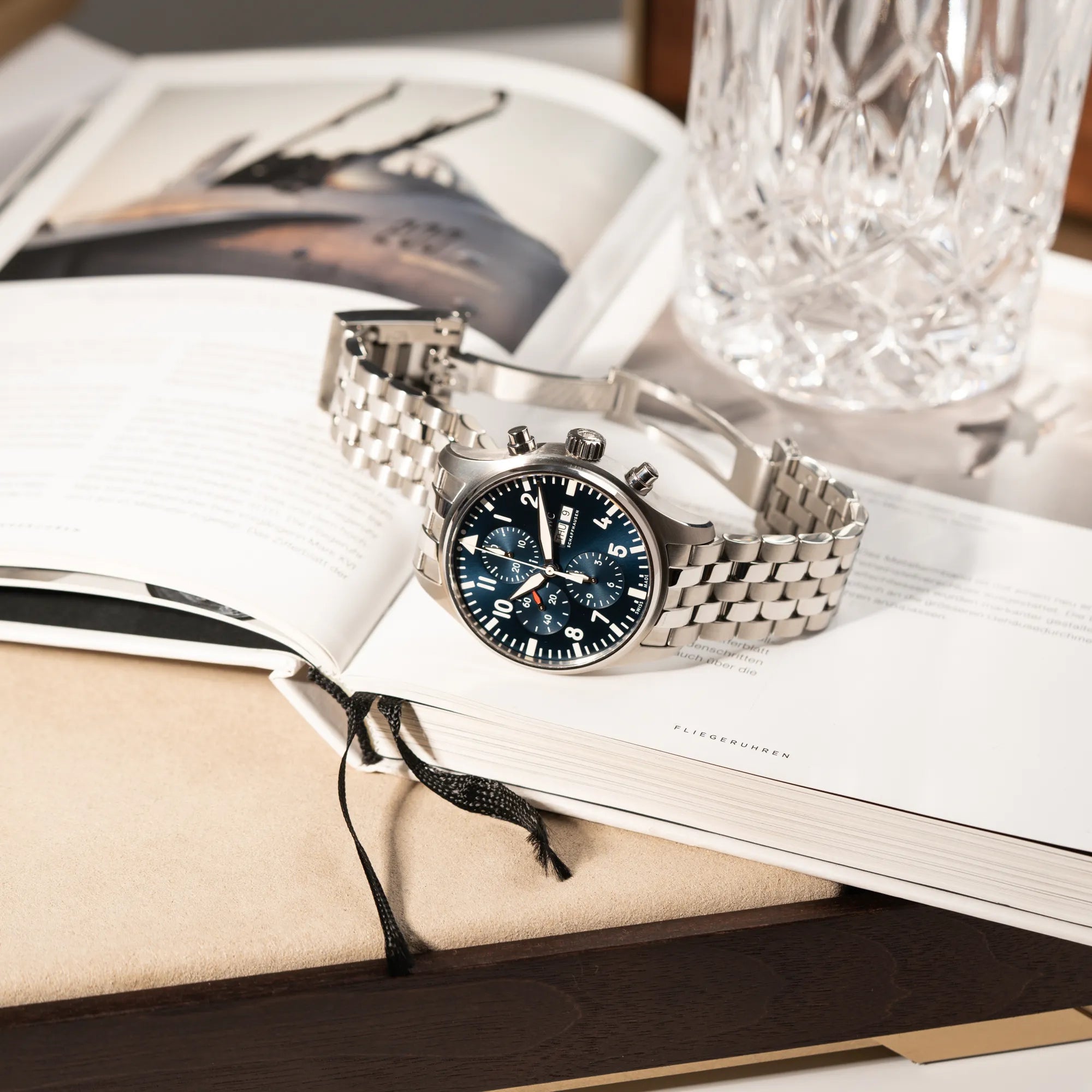 IWC Pilot Chronograph "Le Petit Prince" IW377717 mit 43 mm Gehäuse und blauem Zifferblatt am Edelstahl-Armband liegt mit geöffneter Faltschliesse auf einem Buch über Flugzeuge
