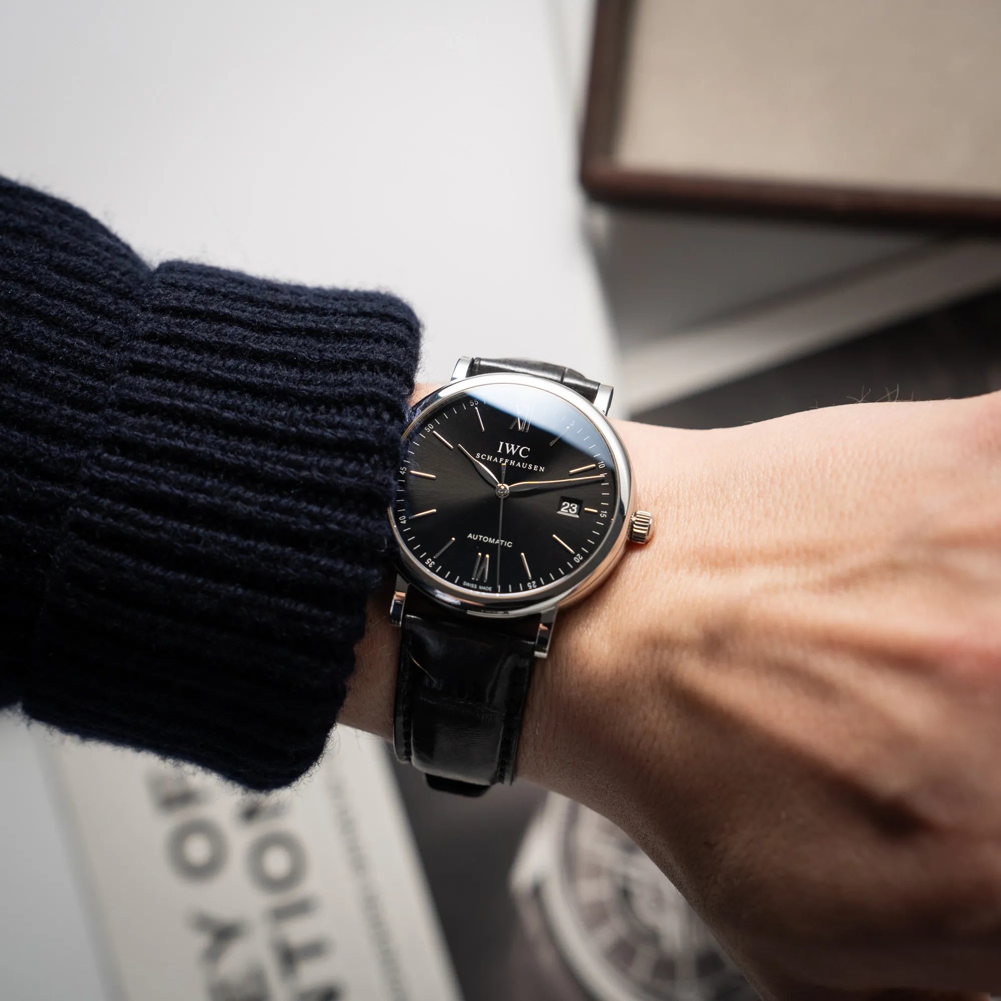 Wristshot mit der IWC Portofino 40 Automatik Armbanduhr mit schwarzem Zifferblatt am schwarzen Lederband an einem Männerhandgelenk