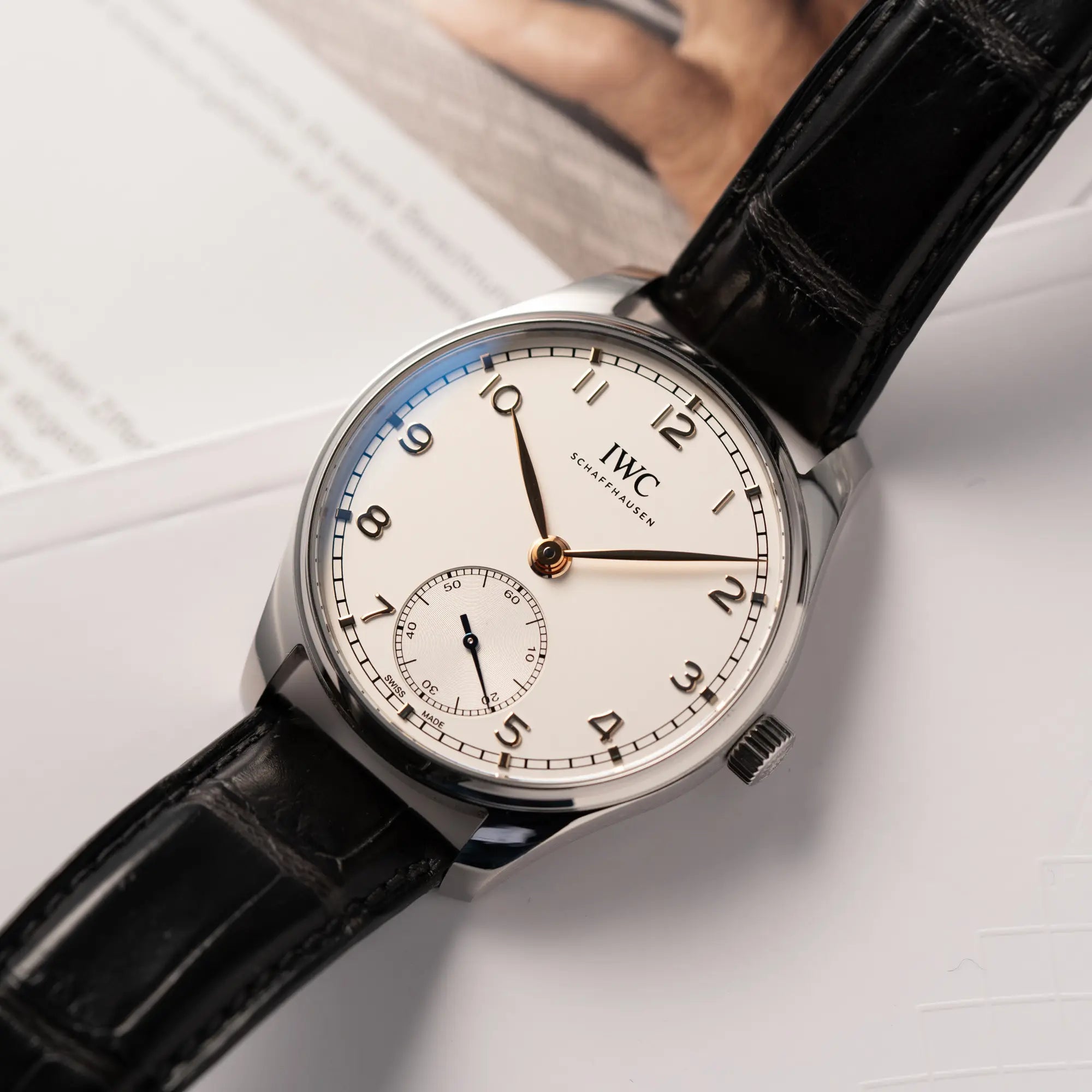 IWC Portugieser 40 Automatik IW358303 mit weißem Zifferblatt und roségoldenen Zeiger- und Index-Details am schwarzen Lederband liegt flach auf einem Uhrenmagazin