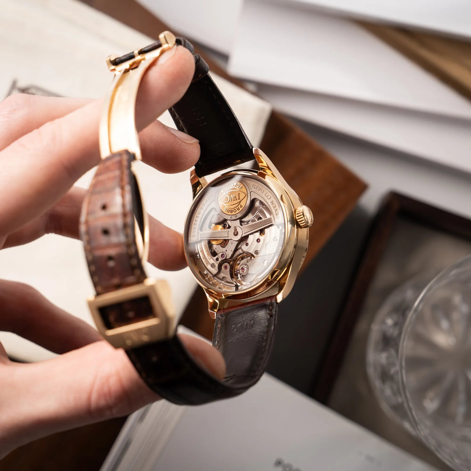 Mann hält den Portugieser Ewiger Kalender IW502213 von IWC in einem 42mm-Rosegold-Gehäuse am braunem IWC Lederband mit einem sanften weißem Zifferblatt in seiner Hand und präsentiert das Uhrwerk durch den gläsernen Gehäuseboden