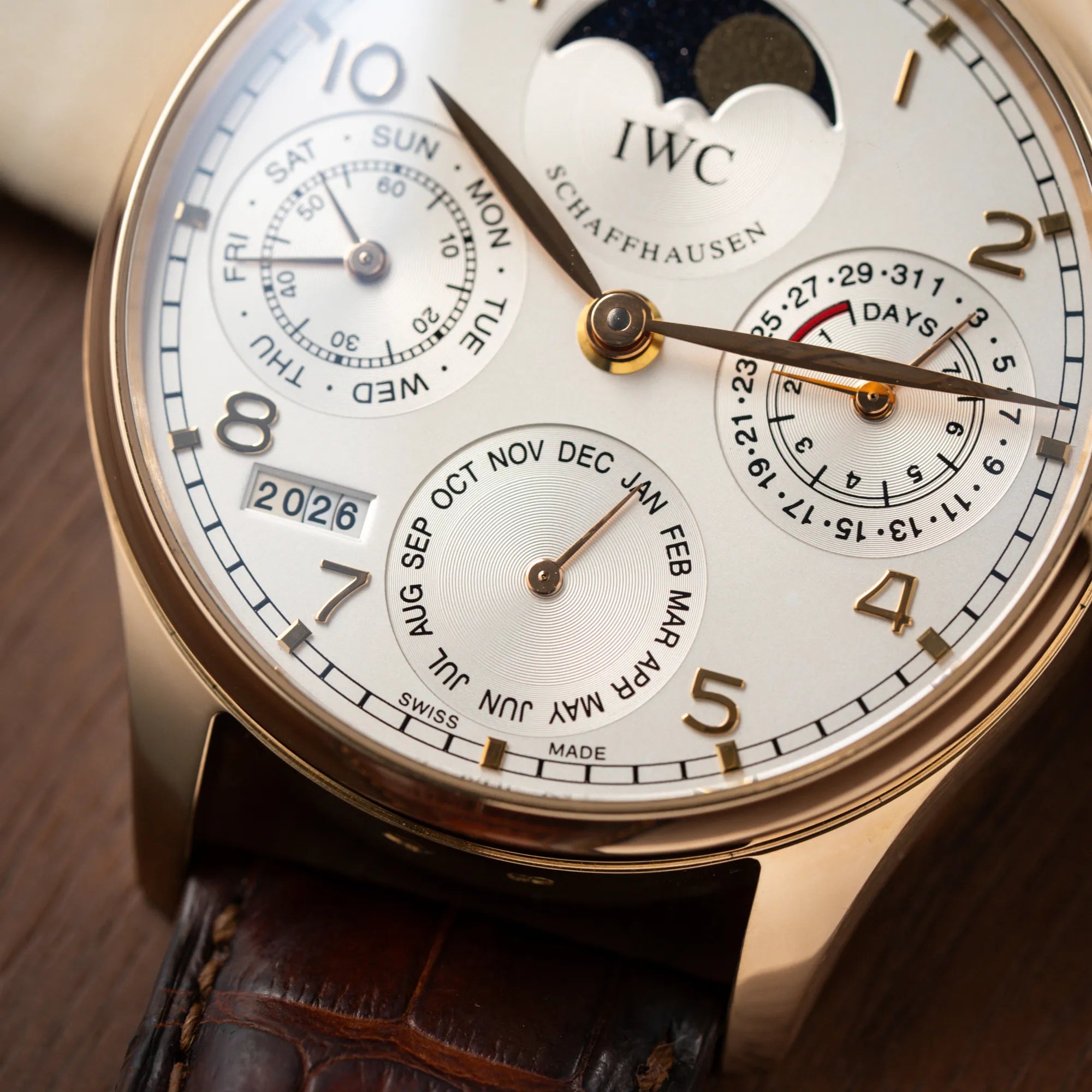 Detailaufnahme mit Fokus auf der Monatsanzeige auf 6 Uht von dem Portugieser Ewiger Kalender IW502213 von IWC in einem 42mm-Rosegold-Gehäuse am braunem IWC Lederband mit einem sanften weißem Zifferblatt