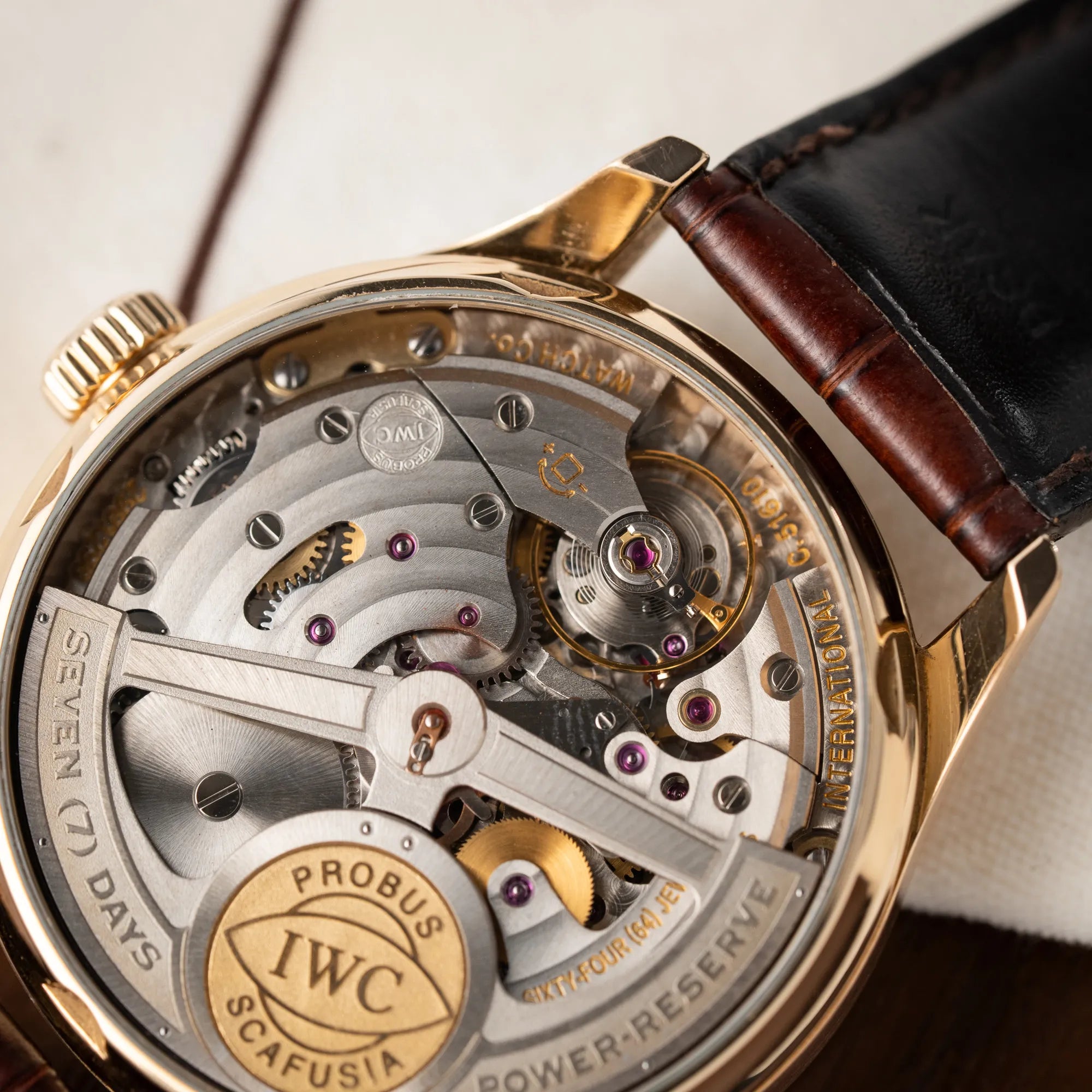 Produktfotografie zeigt das komplizierte Automatik-Uhrwerk des Portugieser Ewiger Kalender IW502213 von IWC in einem 42mm-Rosegold-Gehäuse am braunem IWC Lederband mit einem sanften weißem Zifferblatt durch den gläsernen Gehäuseboden