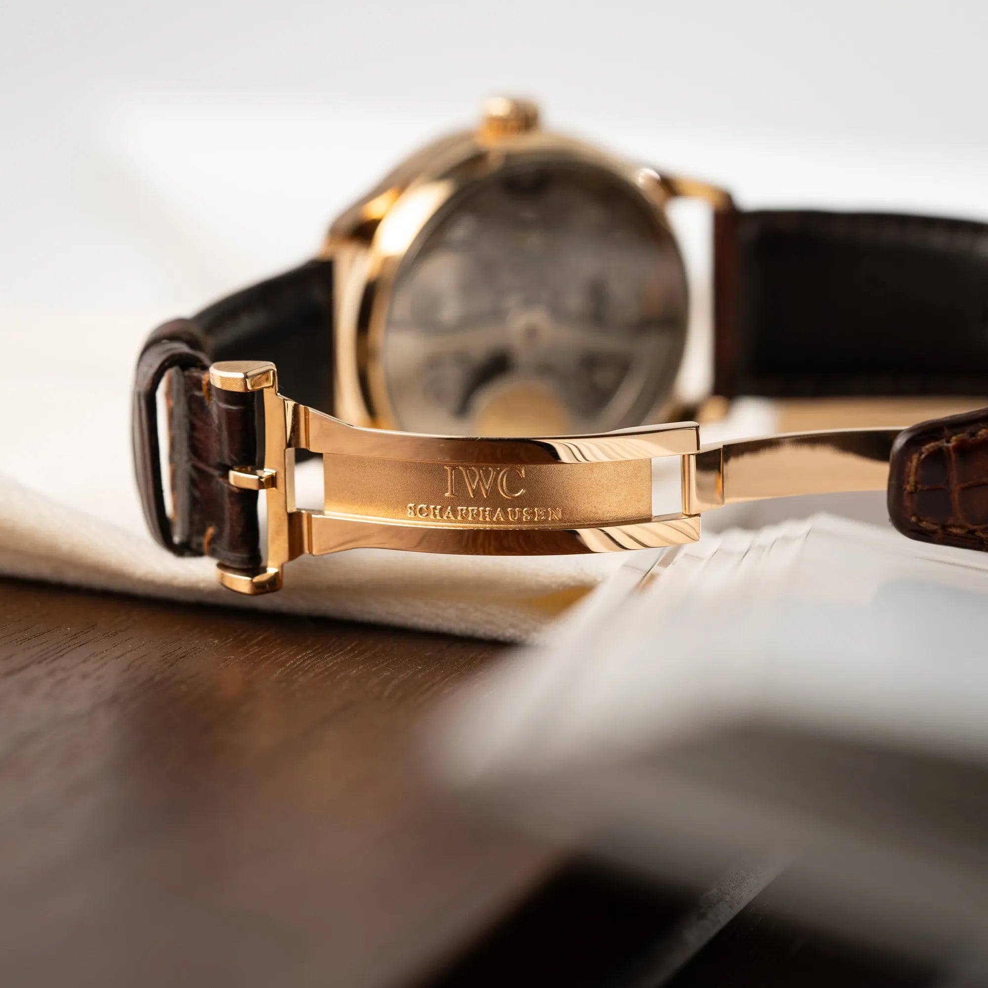 Produktfotografie des Portugieser Ewiger Kalender IW502213 von IWC in einem 42mm-Rosegold-Gehäuse am braunem IWC Lederband mit einem sanften weißem Zifferblatt zeigt die roségoldene Faltschliesse