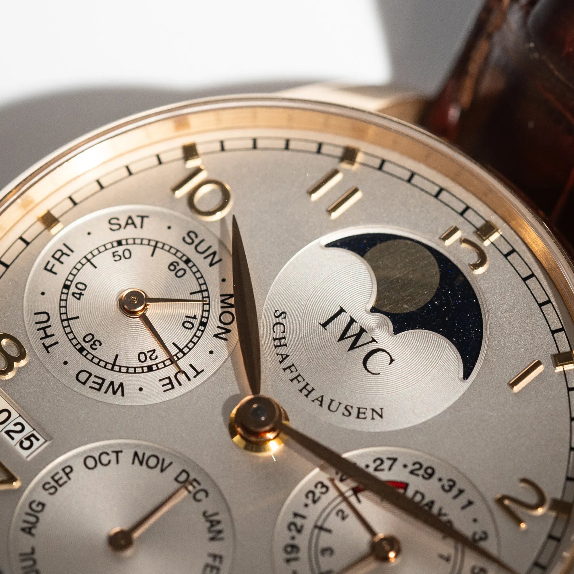 Detailaufnahme des Portugieser Ewiger Kalender IW502213 von IWC in einem 42mm-Rosegold-Gehäuse am braunem IWC Lederband mit einem sanften weißem Zifferblatt