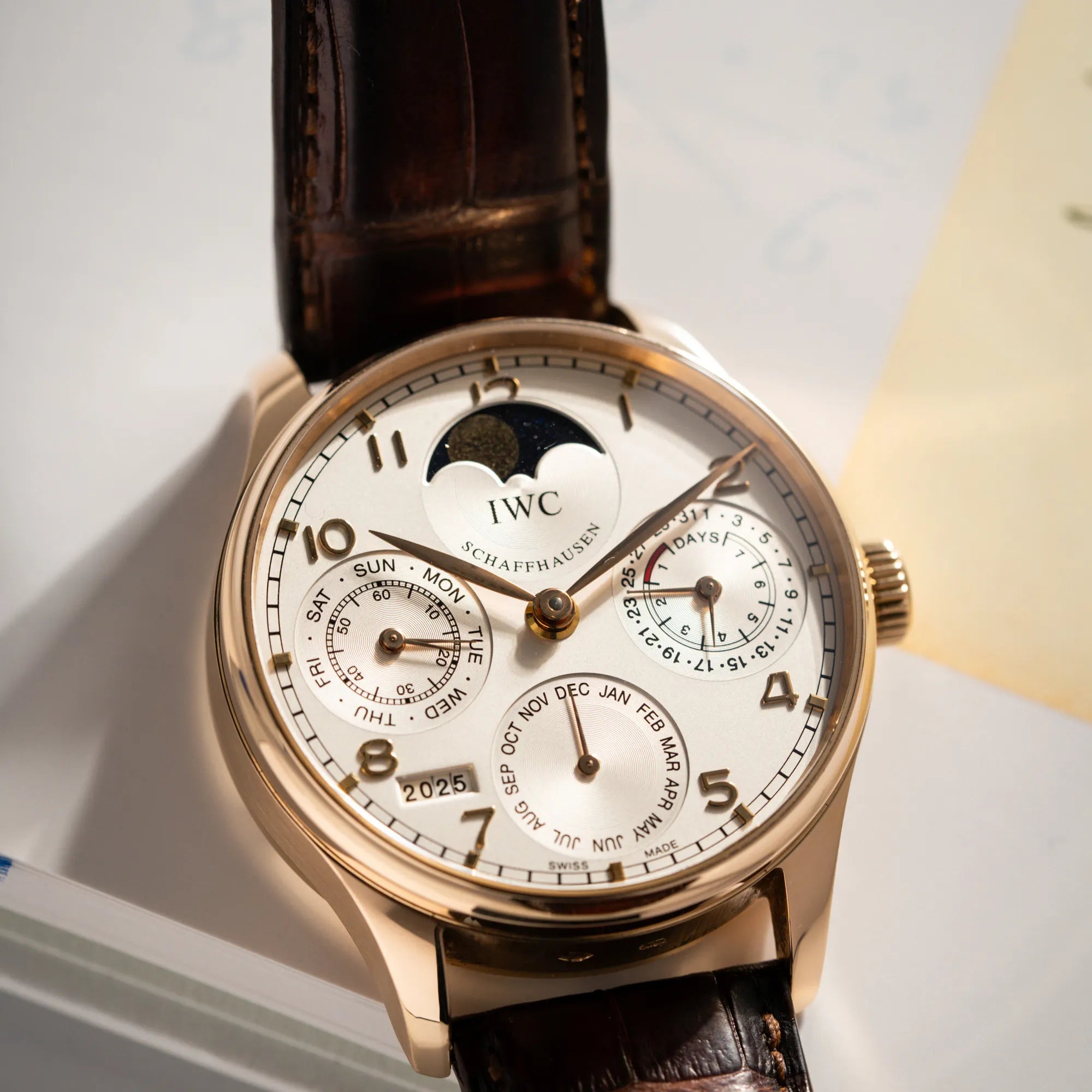 Detailaufnahme des Portugieser Ewiger Kalender IW502213 von IWC in einem 42mm-Rosegold-Gehäuse am braunem IWC Lederband mit einem sanften weißem Zifferblatt