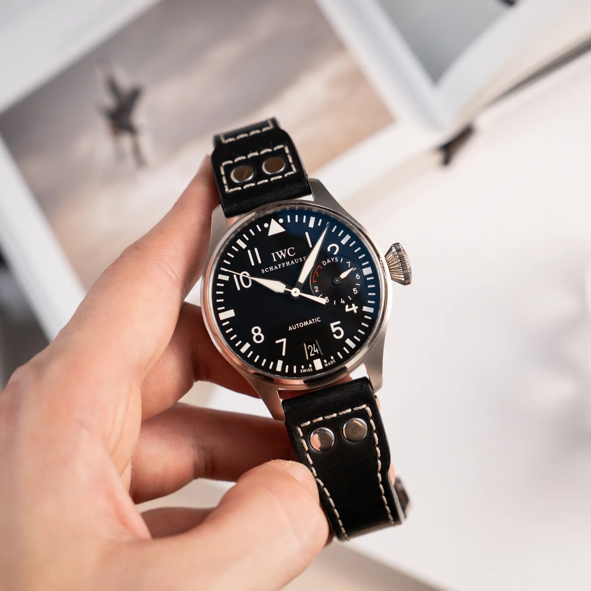 Mann hält die IWC Big Pilot 46 Armbanduhr der Referenz IW500401 mit schwarzem Zifferblatt und der Power-Reserve-Anzeige bei 3 Uhr in seiner Hand und präsentiert die Uhr in die Kamera