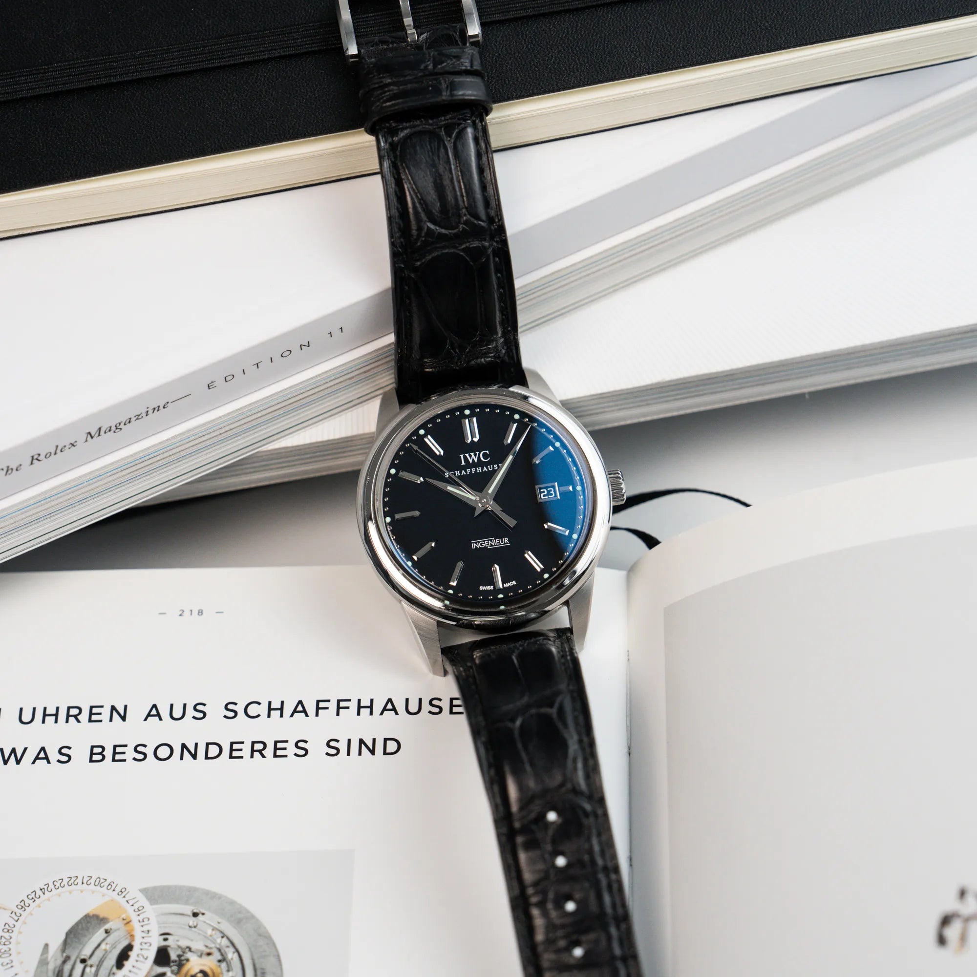 Produktfotografie der IWC Schaffhausen Uhr "Ingenieur" mit der Referenz IW323301 mit schwarzem Zifferblatt, die auf Büchern liegt