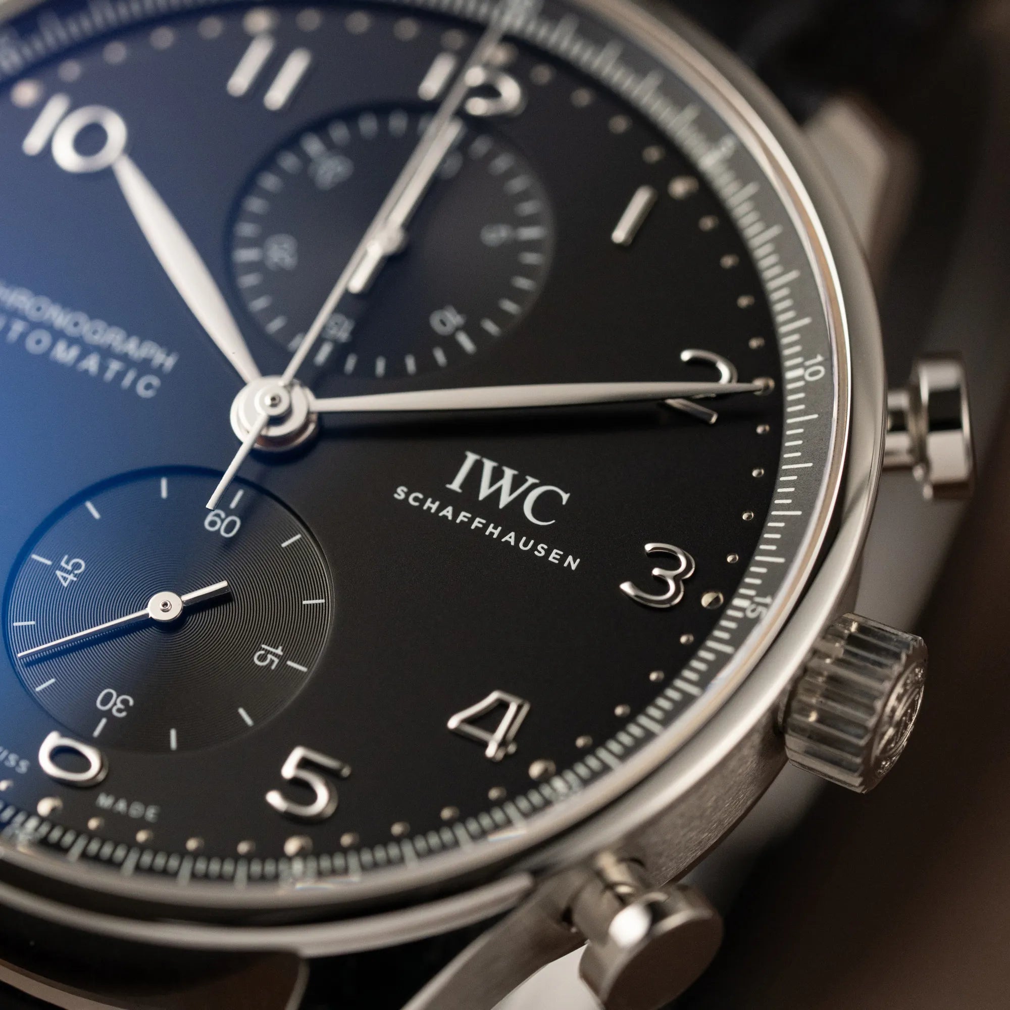 Detailaufnahme der IWC Portugieser Chronograph Uhr mit schwarzem Zifferblatt an einem schwarzen Lederband mit Fokus auf dem Zifferblatt und der Gehäuseoberkante