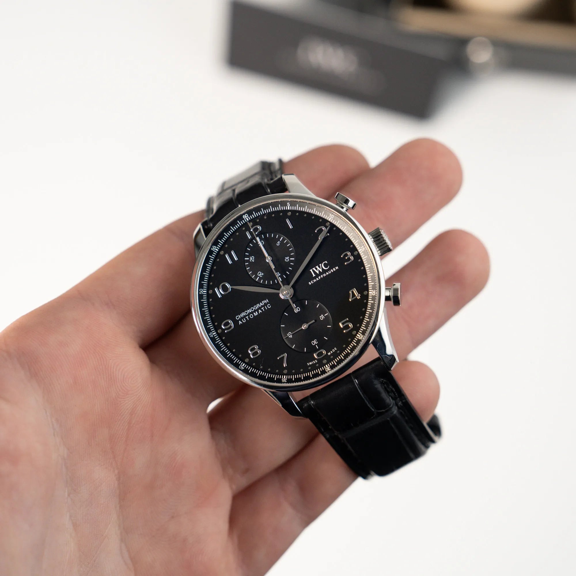 Mann hält die IWC Portugieser Chronograph Uhr mit schwarzem Zifferblatt an einem schwarzen Lederband in seiner Hand