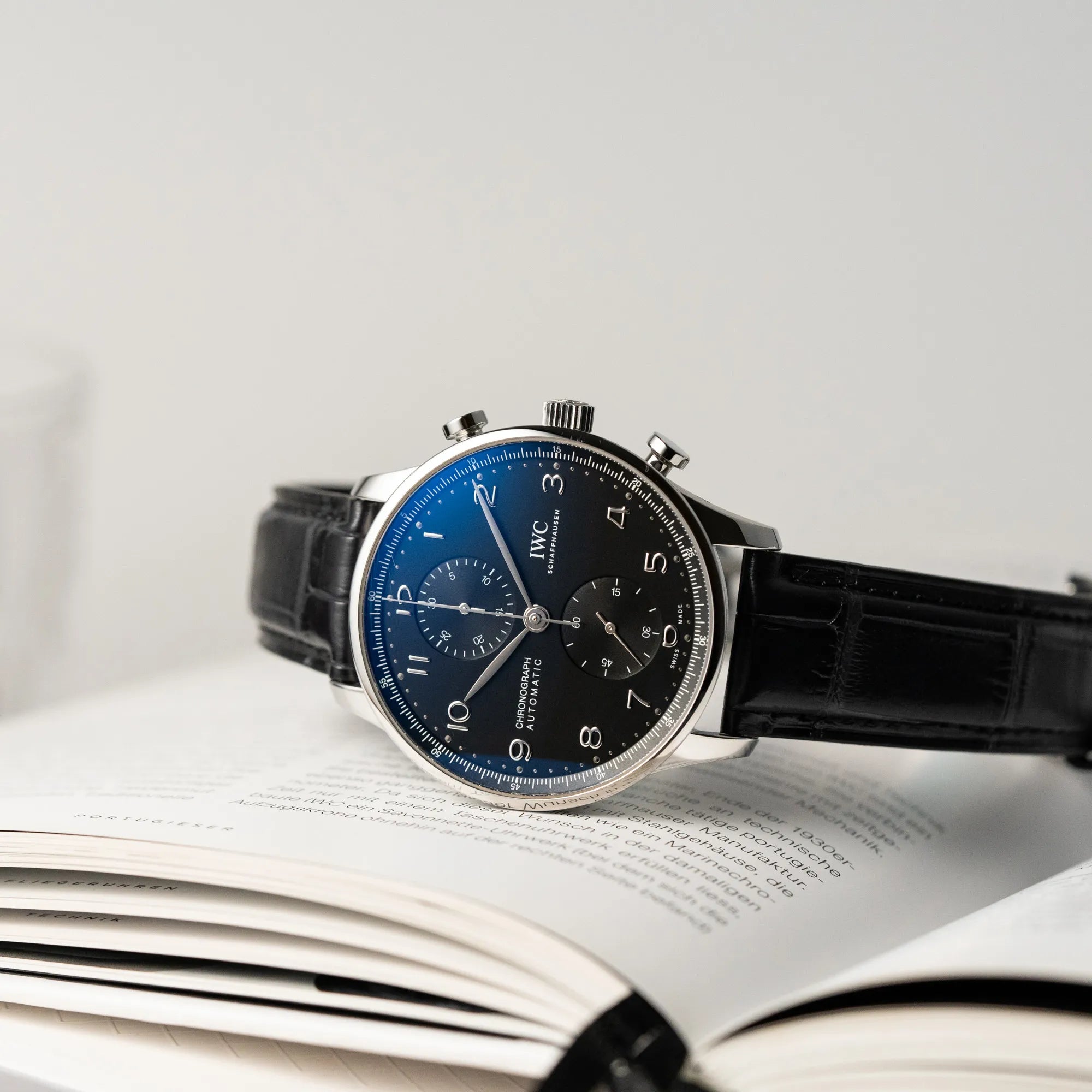 Produktfotografie der IWC Portugieser Chronograph Uhr mit schwarzem Zifferblatt an einem schwarzen Lederband, die die Wirkung des Uhrenglases zeigt