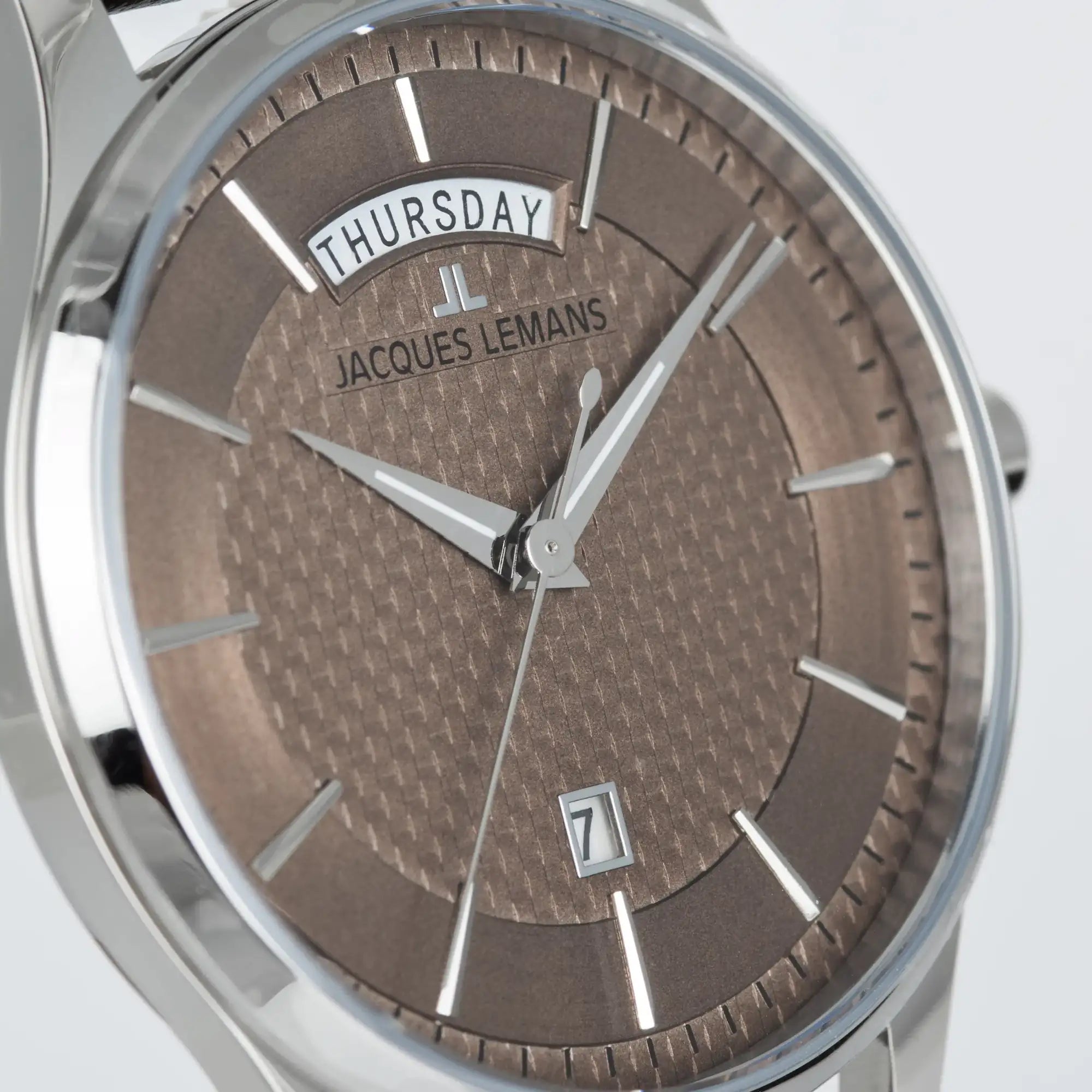 Leicht schräge Ansicht der Jacques Lemans 1-2193K Derby Armbanduhr mit Tages und Datumsanzeige, welche farblich abgestimmt ist durch ein bronzefarbenes Zifferblatt und ein braunes Lederband