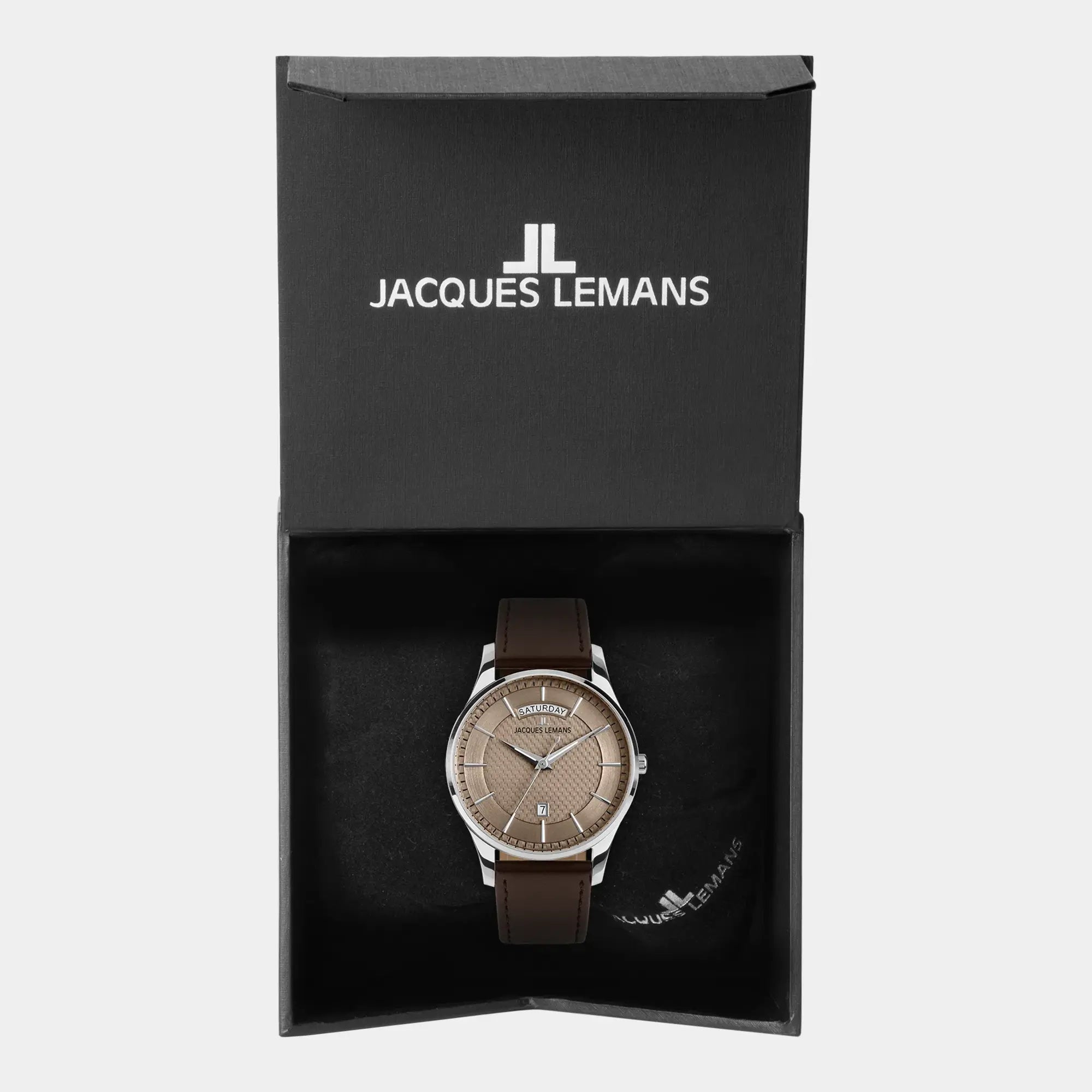 Jacques Lemans 1-2193K Derby Armbanduhr mit Tages und Datumsanzeige, welche farblich abgestimmt ist durch ein bronzefarbenes Zifferblatt und ein braunes Lederband liegt in der zugehörigen Uhrenbox