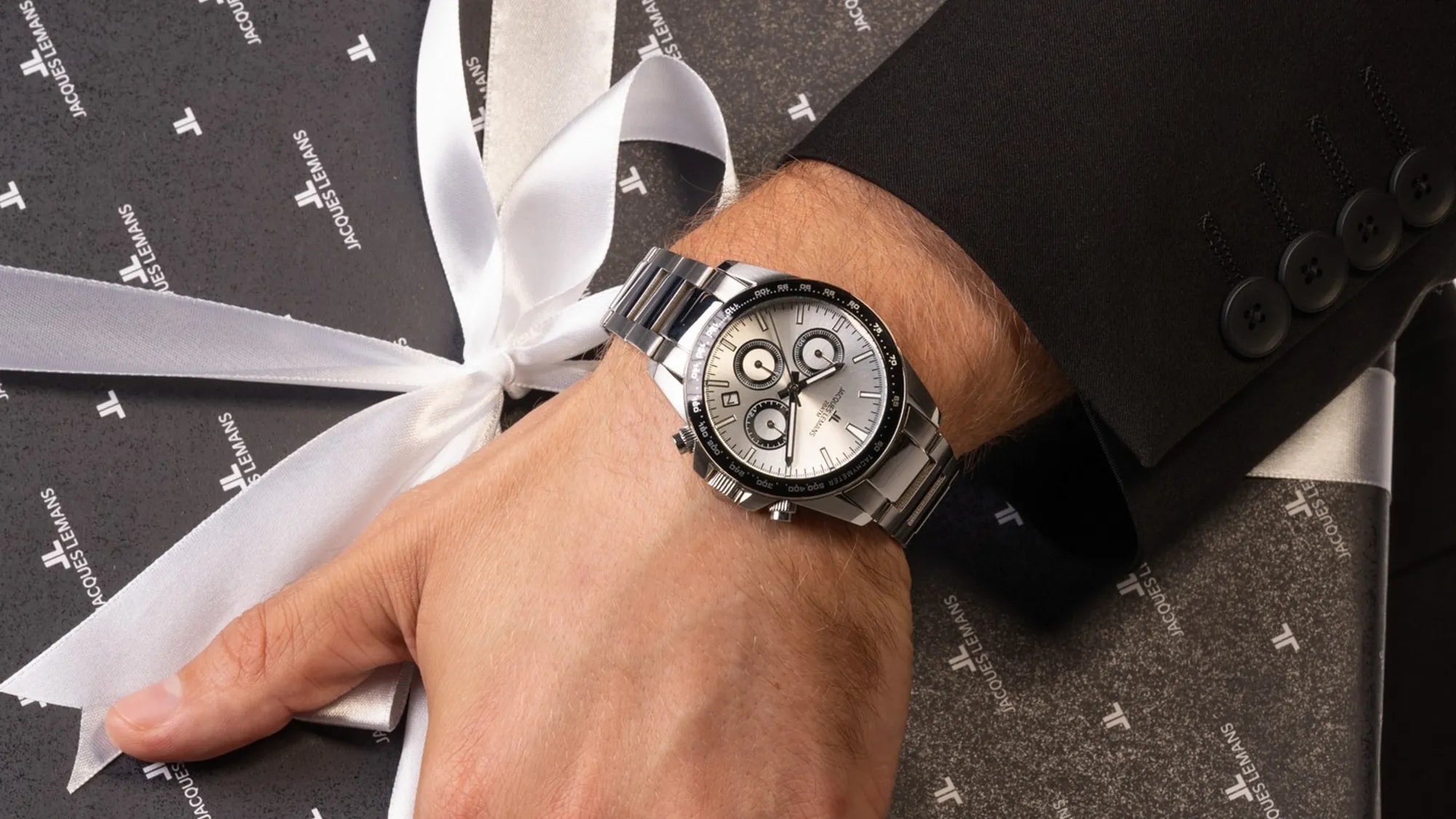 Mann trägt Chronograph von Jacques Lemans aus Edelstahl am Handgelenk und hält ein Jacques Lemans Geschenk unter dem Arm