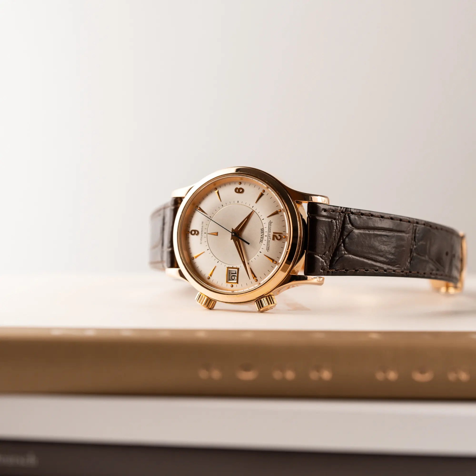 Produktfotografie der auf den zwei Aufzugskronen liegenden Jaeger-LeCoultre Master Memovox 141.2.97 Armbanduhr in Rosegold mit braunem Lederband