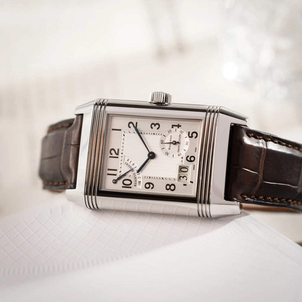 Produktfotografie der Jaeger-LeCoultre Reverso Grande Date der Referenz 240.8.15 mit silberfarbenem Zifferblatt und Großdatums-Anzeige, kleiner Sekunde und Gangreserve-Anzeige am braunen Lederband
