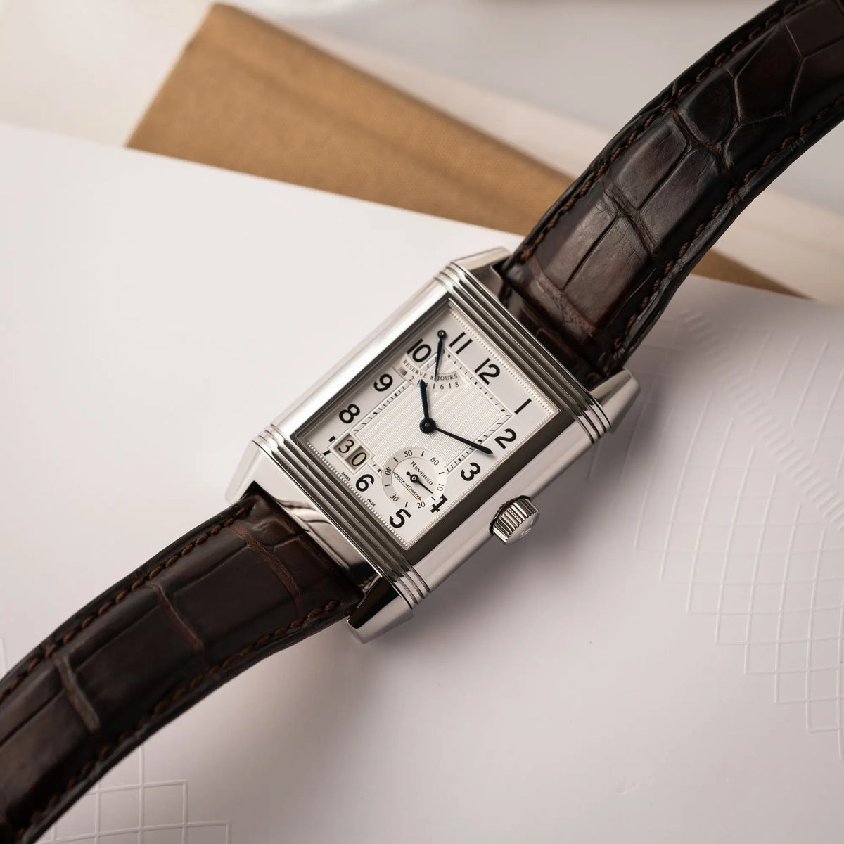 Produktfotografie der Jaeger-LeCoultre Reverso Grande Date der Referenz 240.8.15 mit silberfarbenem Zifferblatt und Großdatums-Anzeige, kleiner Sekunde und Gangreserve-Anzeige am braunen Lederband