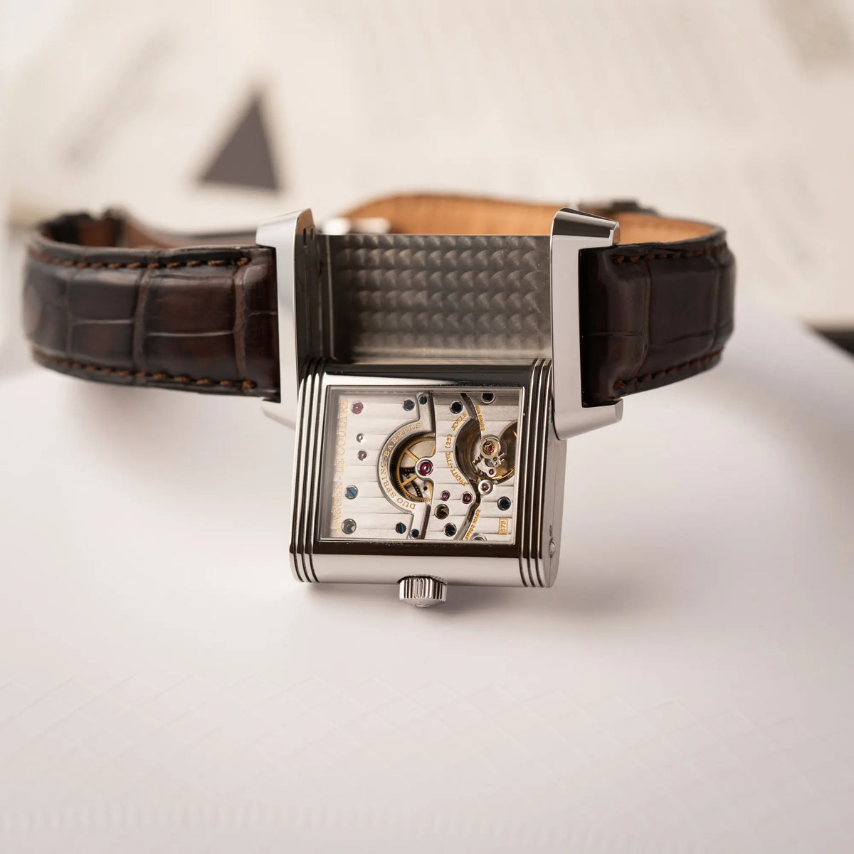 Produktfotografie zeigt die Jaeger-LeCoultre Reverso Grande Date der Referenz 240.8.15 mit silberfarbenem Zifferblatt und Großdatums-Anzeige, kleiner Sekunde und Gangreserve-Anzeige am braunen Lederband, während der Reverso-Mechanismus betätigt wurde und das Handaufzug-Kaliber 