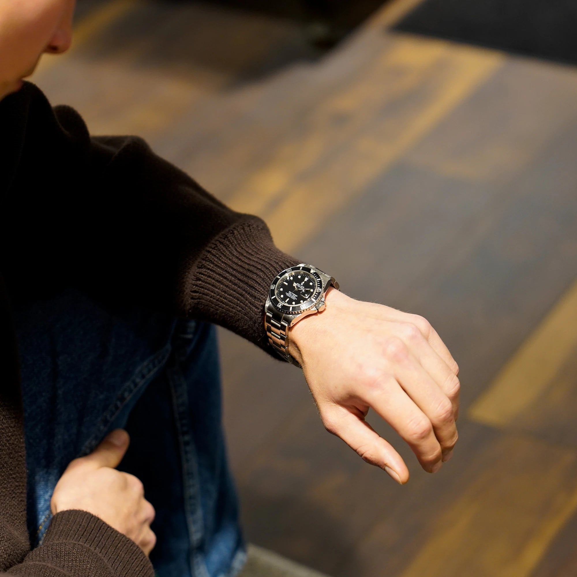 Mann trägt die Rolex Submariner Date in schwarz, Referenz 16610, mit Flat-Four-Lünette am Handgelenk und schaut sich die Uhr an