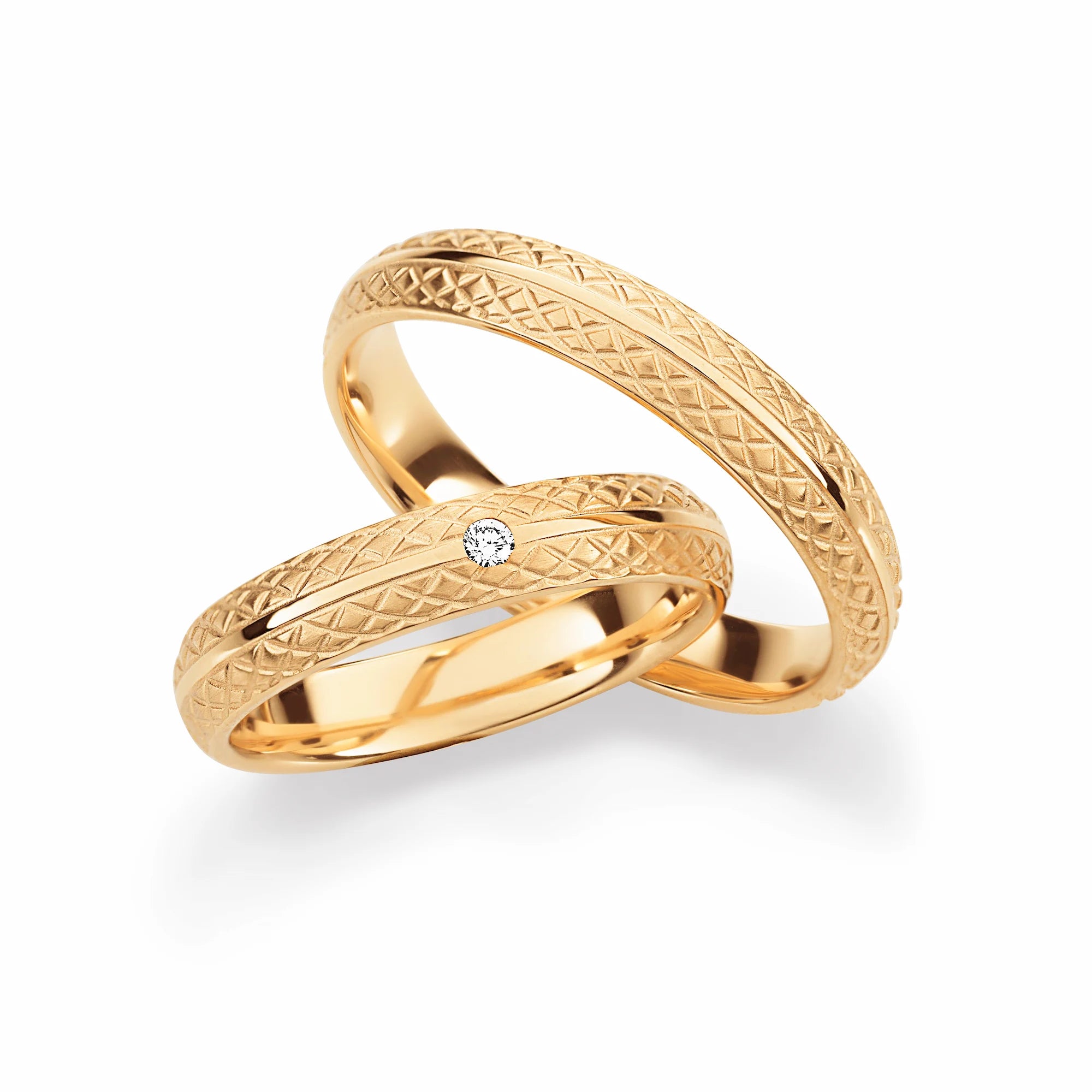 Produktfotografie des gelbgoldenen Max Kemper Trauringpaars mit einem feinem Muster und einem mittigen, polierten Zierstand und einem zentralen Diamanten beim Damenring