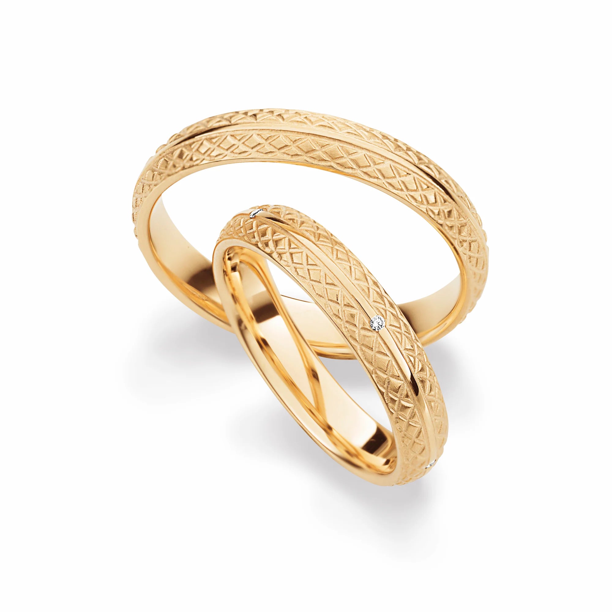 Produktfotografie des gelbgoldenen Max Kemper Trauringpaars mit gravierter, gemusterter Oberfläche und einem mittig durchgezogenen, hochpolierten Zierstreifen, auf dem für den Damenring Brillanten eingesetzt wurden