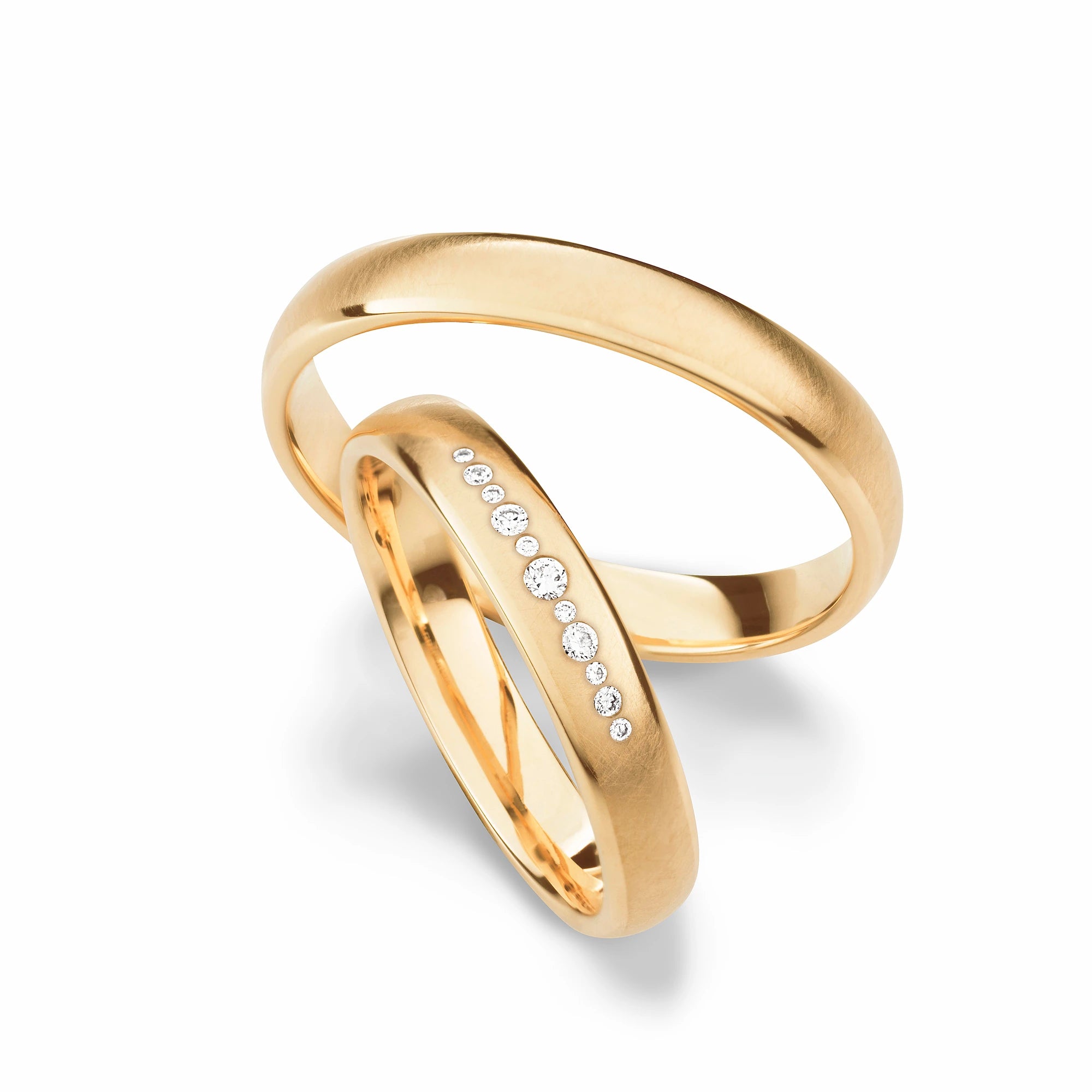 Produktfotografie des gelbgoldenen Max Kemper Trauringpaars mit einer galtt strukturierten Oberfläche und einer Reihe an Diamanten im Damenring
